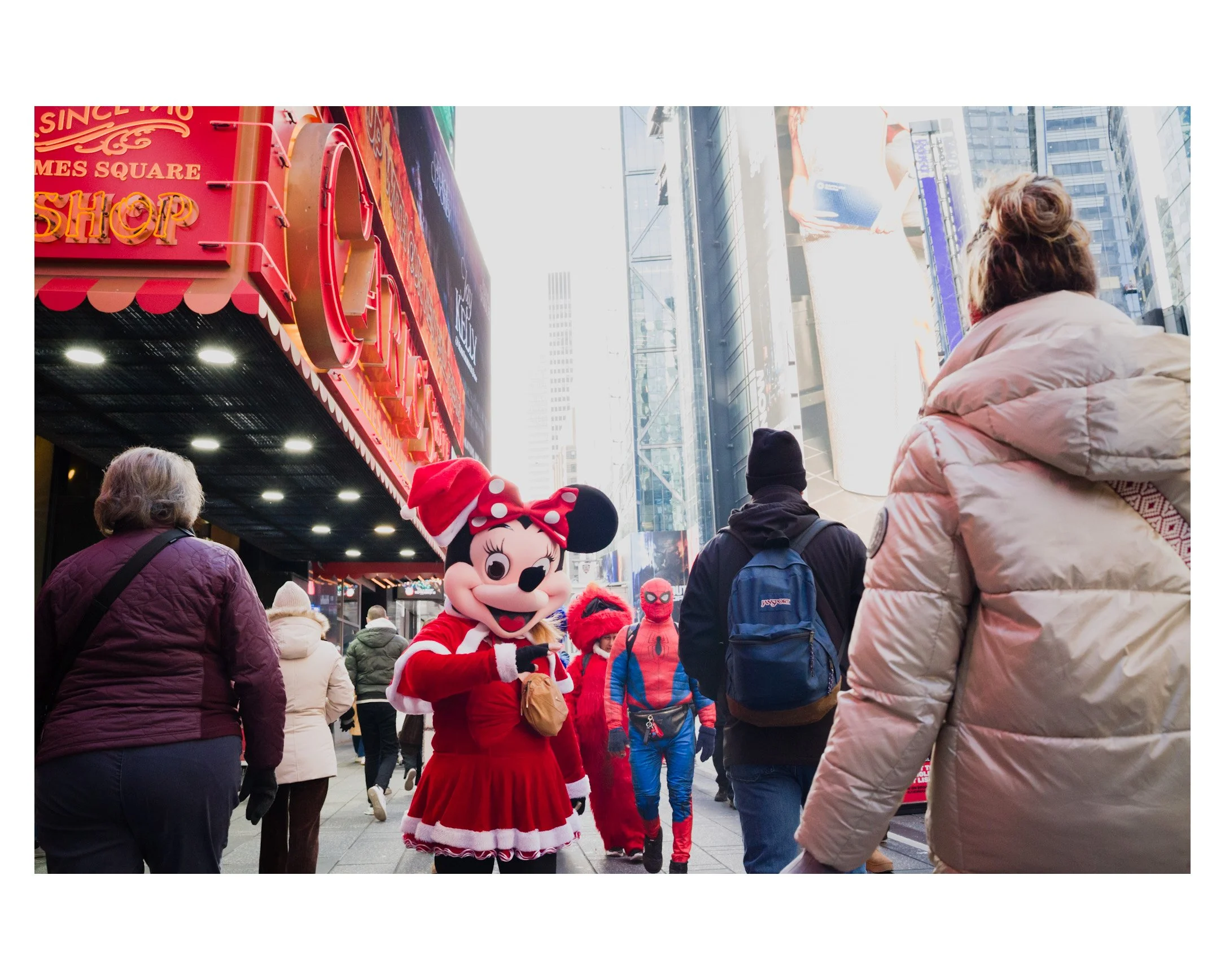 People walking in Times Square with Minnie Mouse mascot dressed in a Christmas outfit and others in costumes including Spider-Man.
