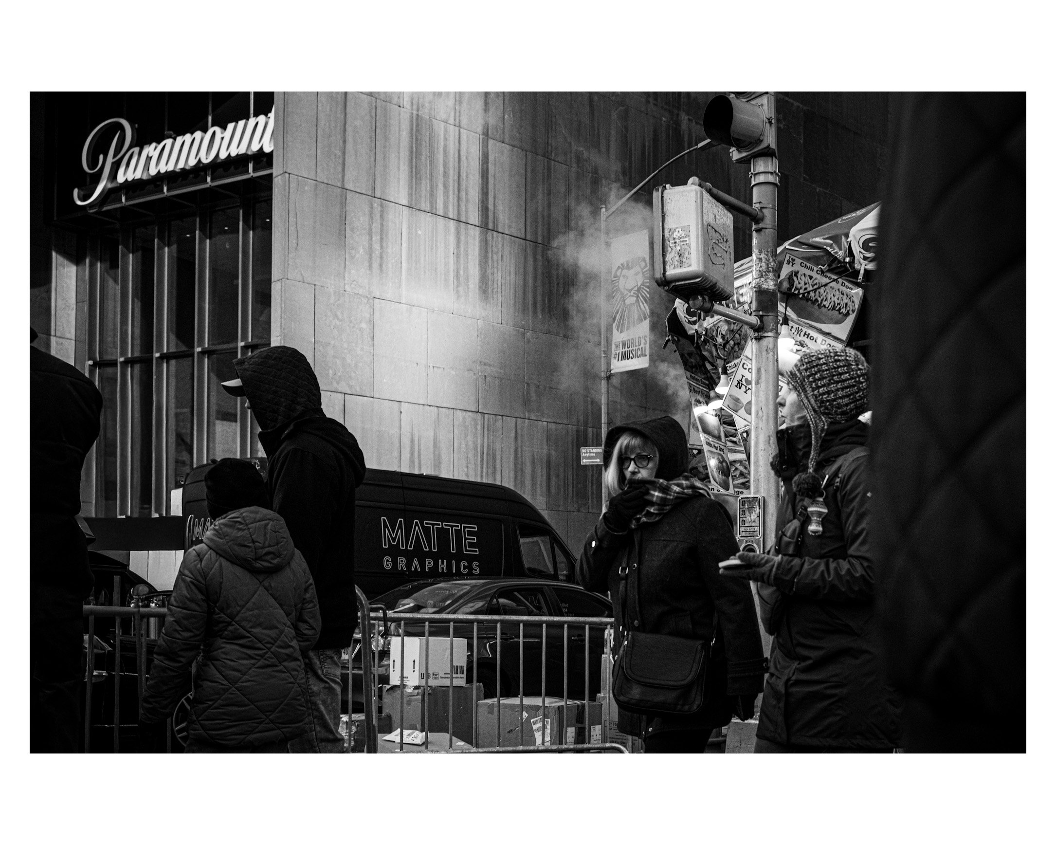 People in winter clothing standing on a city sidewalk in front of a Paramount theater.
