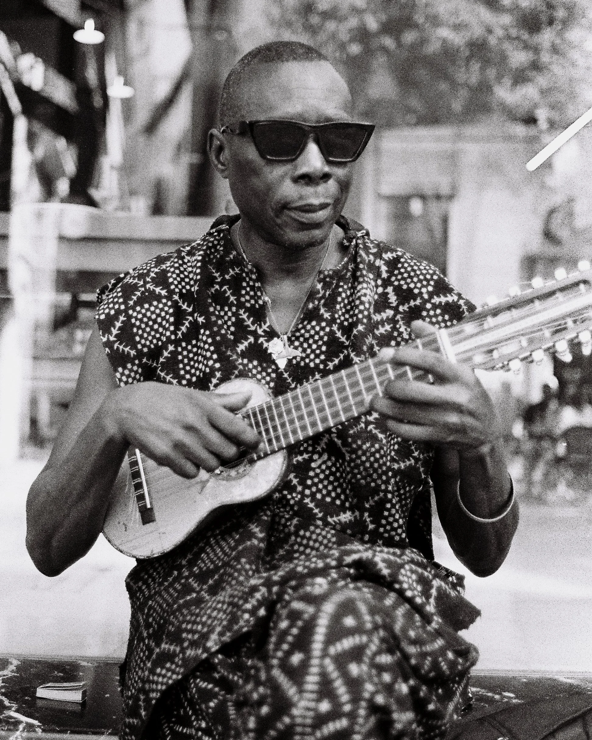 A person wearing sunglasses and patterned clothing playing a ukulele.