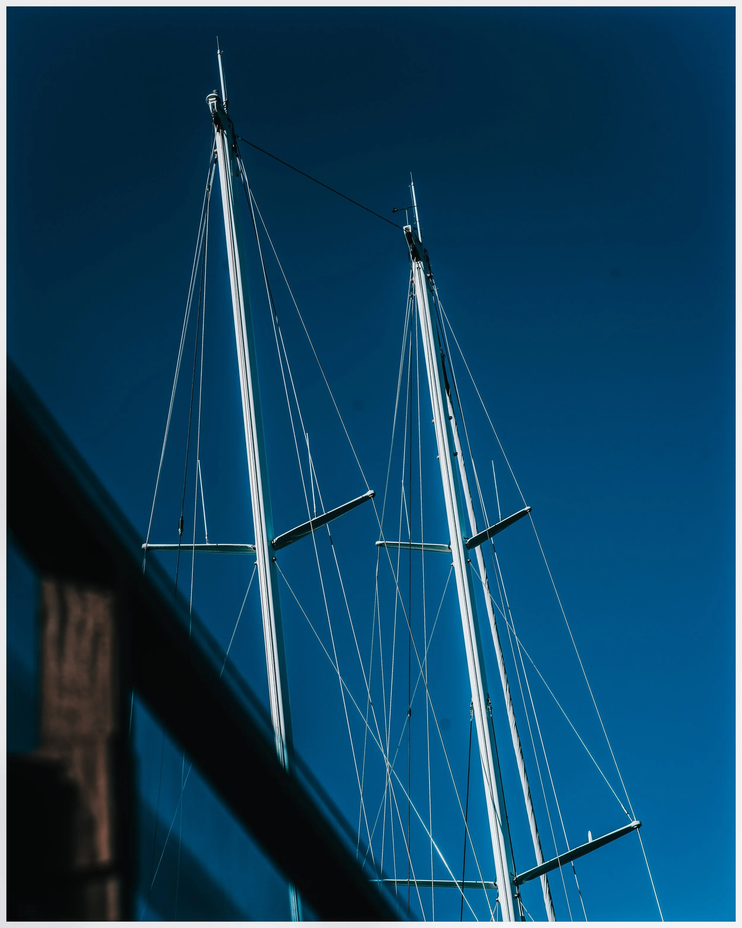 Close-up view of two tall yacht masts with rigging against a clear blue sky.