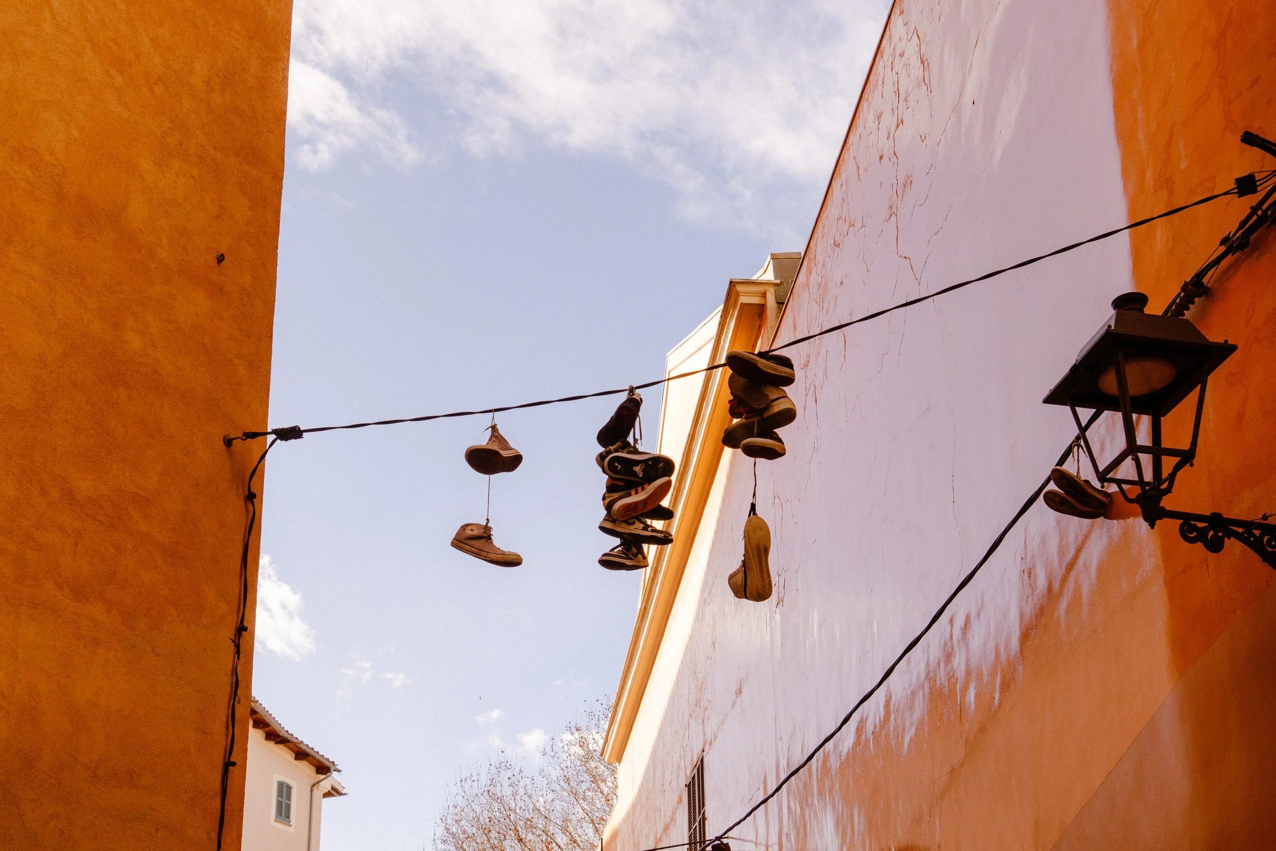 Shoes hanging on a clothesline between two colorful buildings, with a blue sky and clouds in the background.
