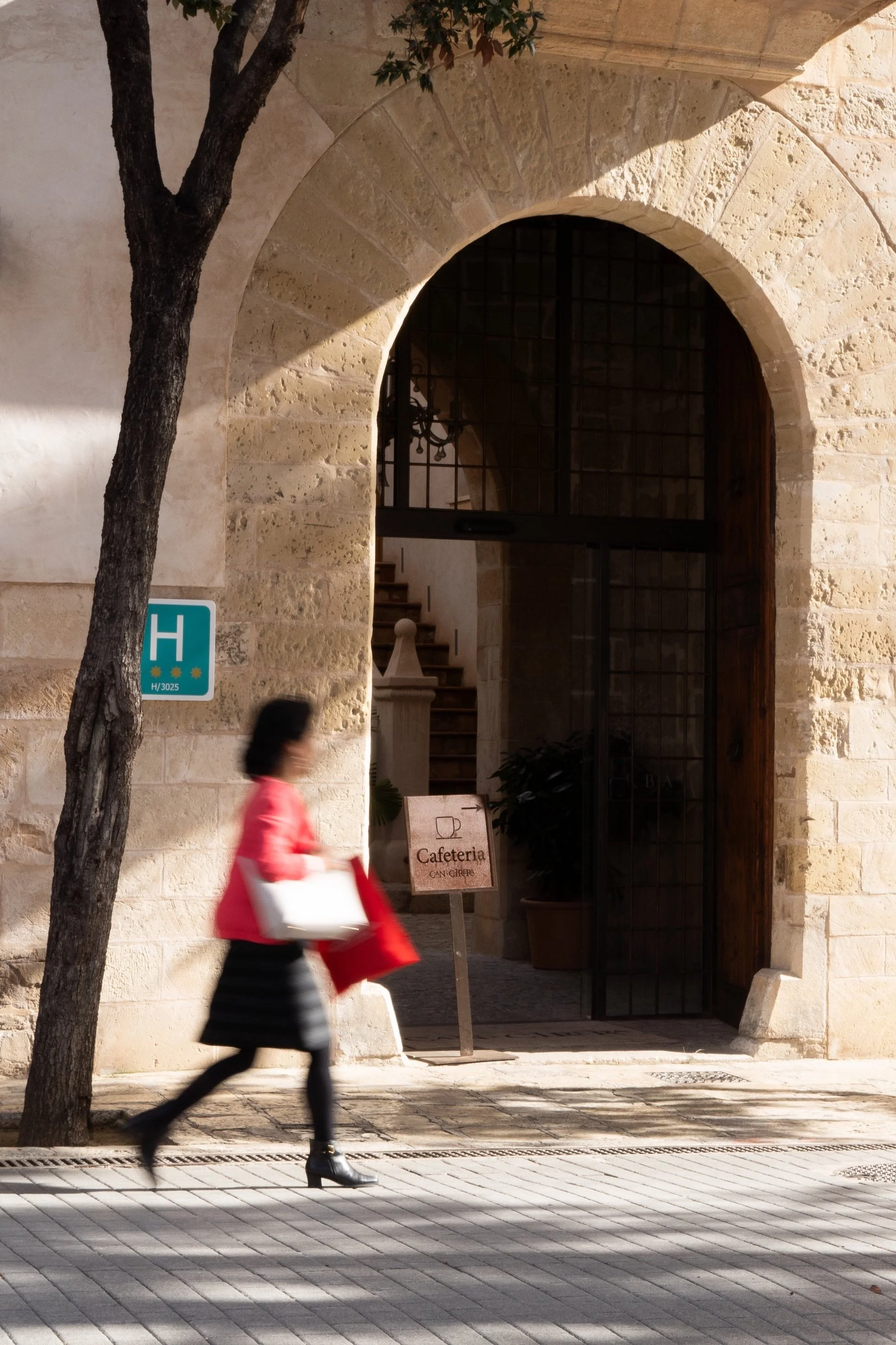 Blurred person walking past a stone archway with a sign for a cafeteria, and a green hotel sign on the wall.