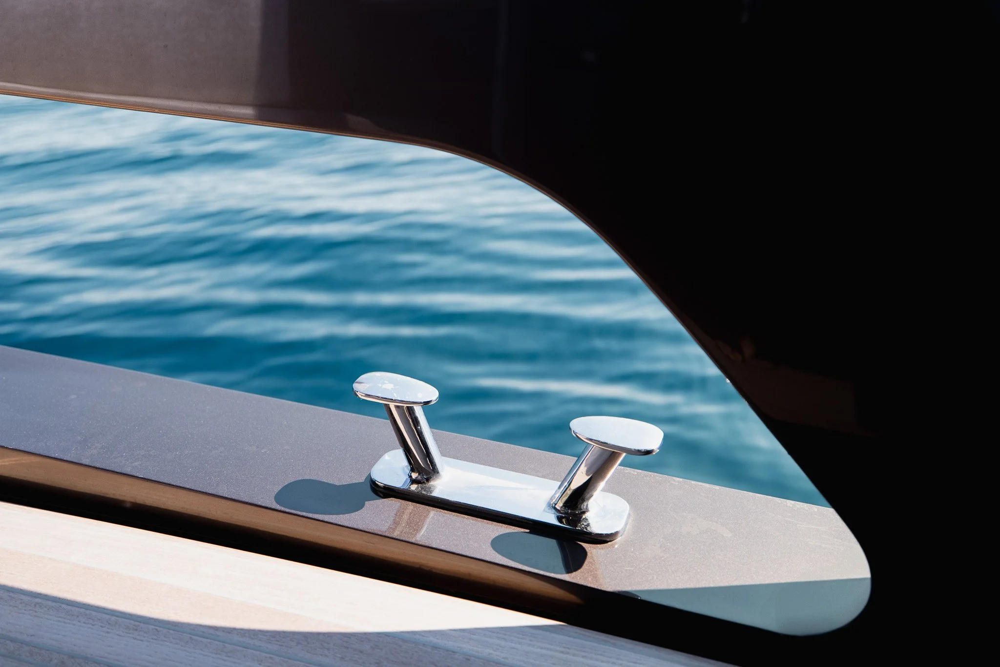 Close-up of a shiny metal cleat on the side of a boat, with water in the background.