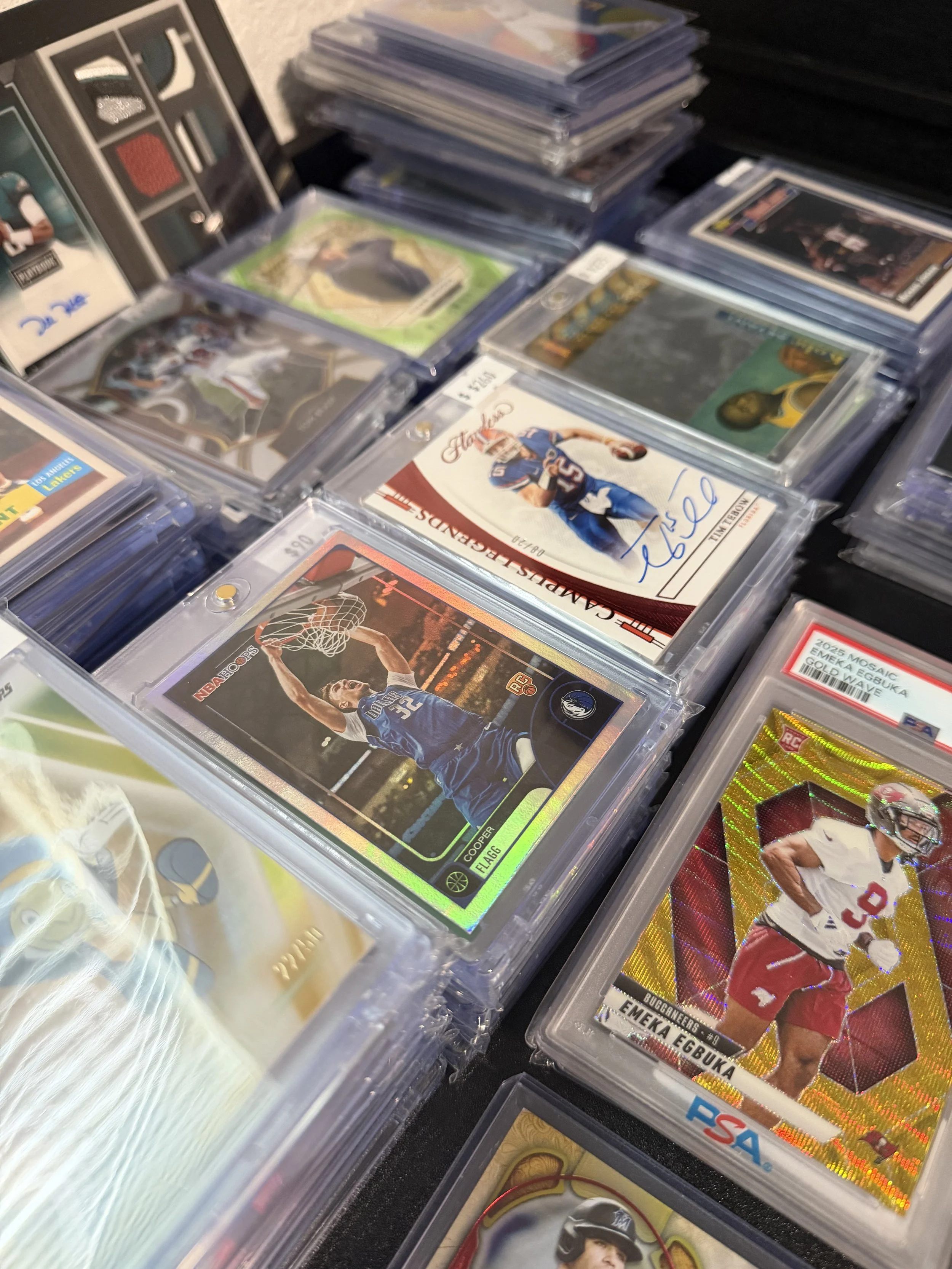 A collection of sports trading cards in plastic cases, featuring athletes from various sports including football, basketball, and baseball, displayed on a table.