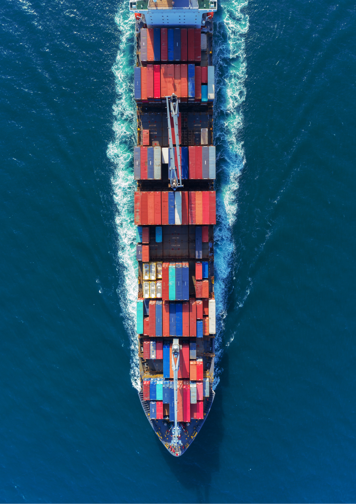 Overhead view of a cargo ship sailing through the ocean, loaded with multicolored containers.