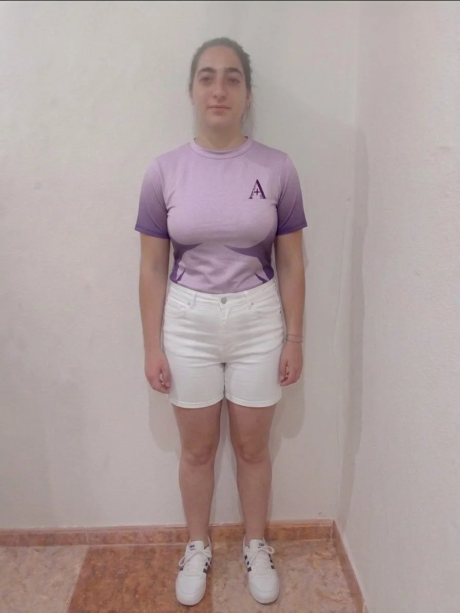 Juvenil con control de condición física, con camiseta lila con letras negras en el lado izquierdo del pecho y pantalones cortos blancos, calzando deportivos blancos, en una pared blanca