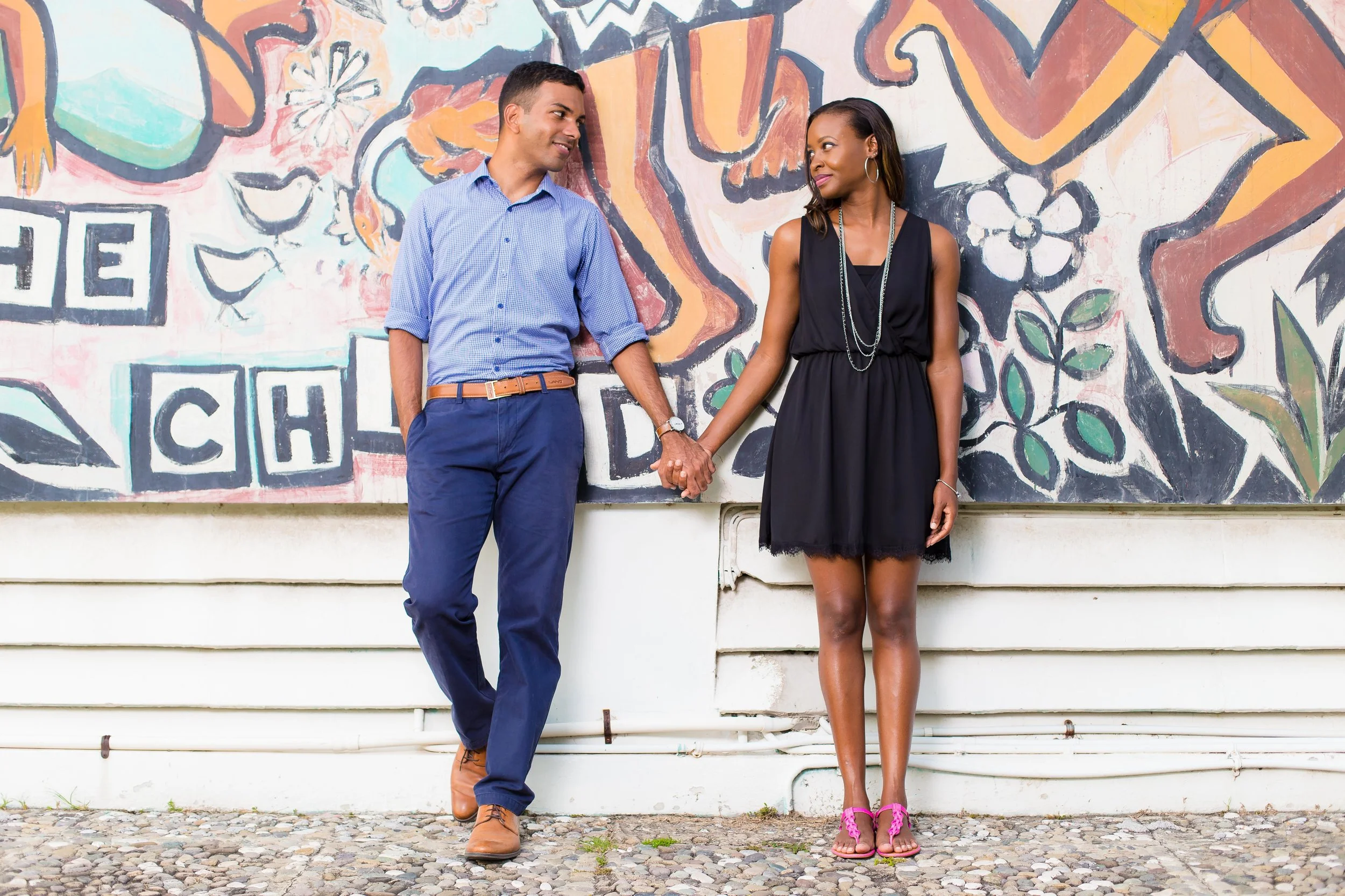 A man and woman holding hands and looking at each other while standing in front of a colorful mural wall.