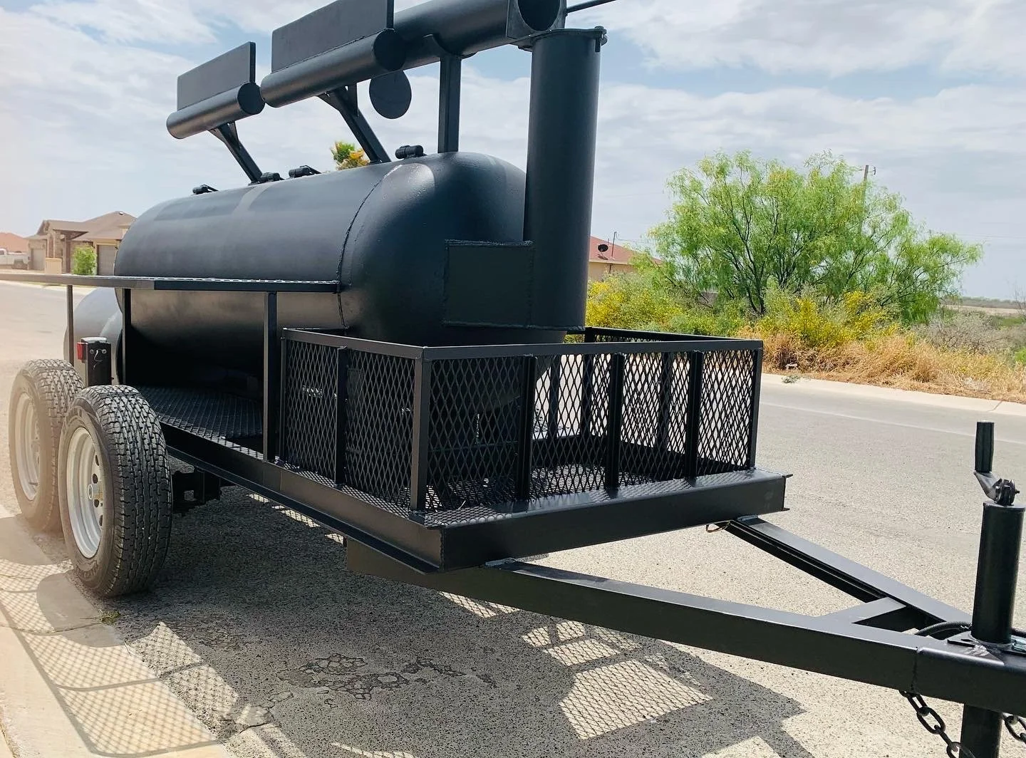 Black barbecue smoker on a trailer parked on a street with a tree in the background.