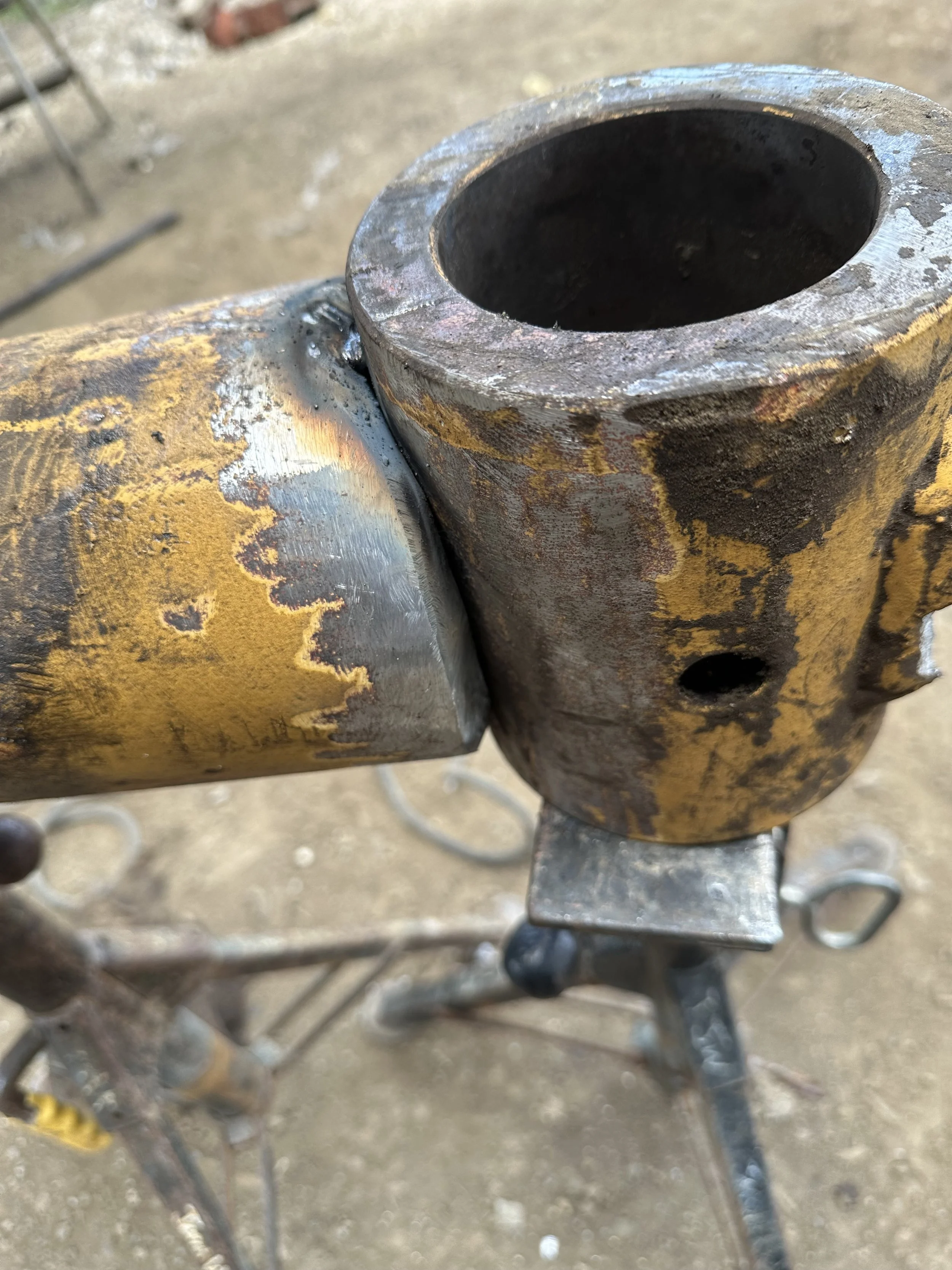 Close-up of a metal pipe joint with visible rust and welding marks, part of a piece of equipment or machinery.
