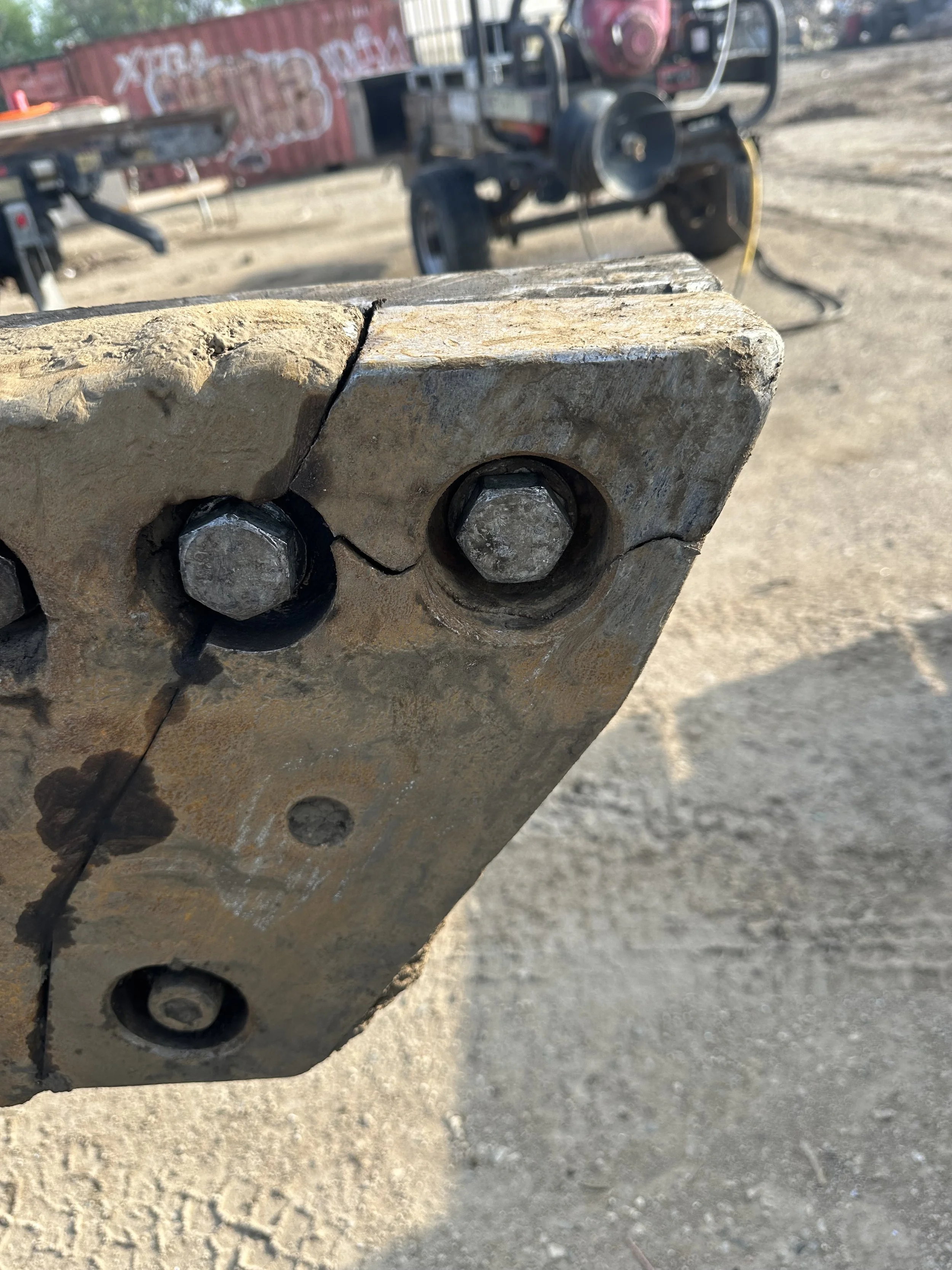 Close-up of a rusty metal connecting plate with bolts, with a construction site in the background and a red trailer.