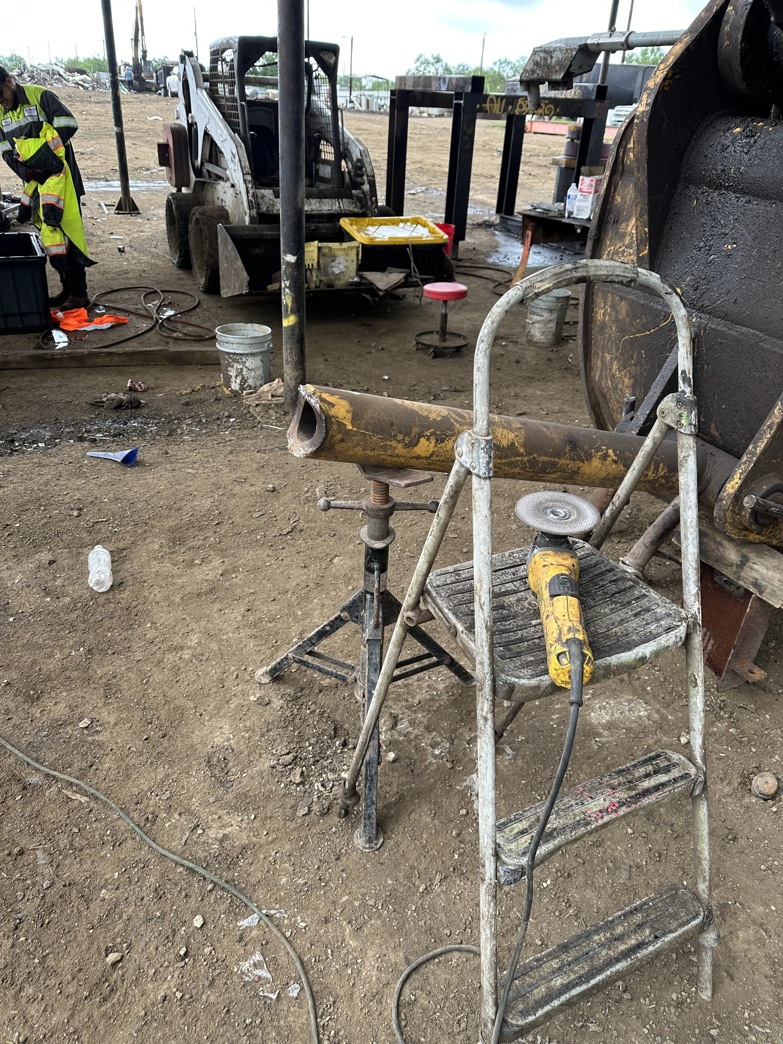 Construction site with a bare dirt ground, construction machinery, work tools, and workers dressed in safety vests and gear.