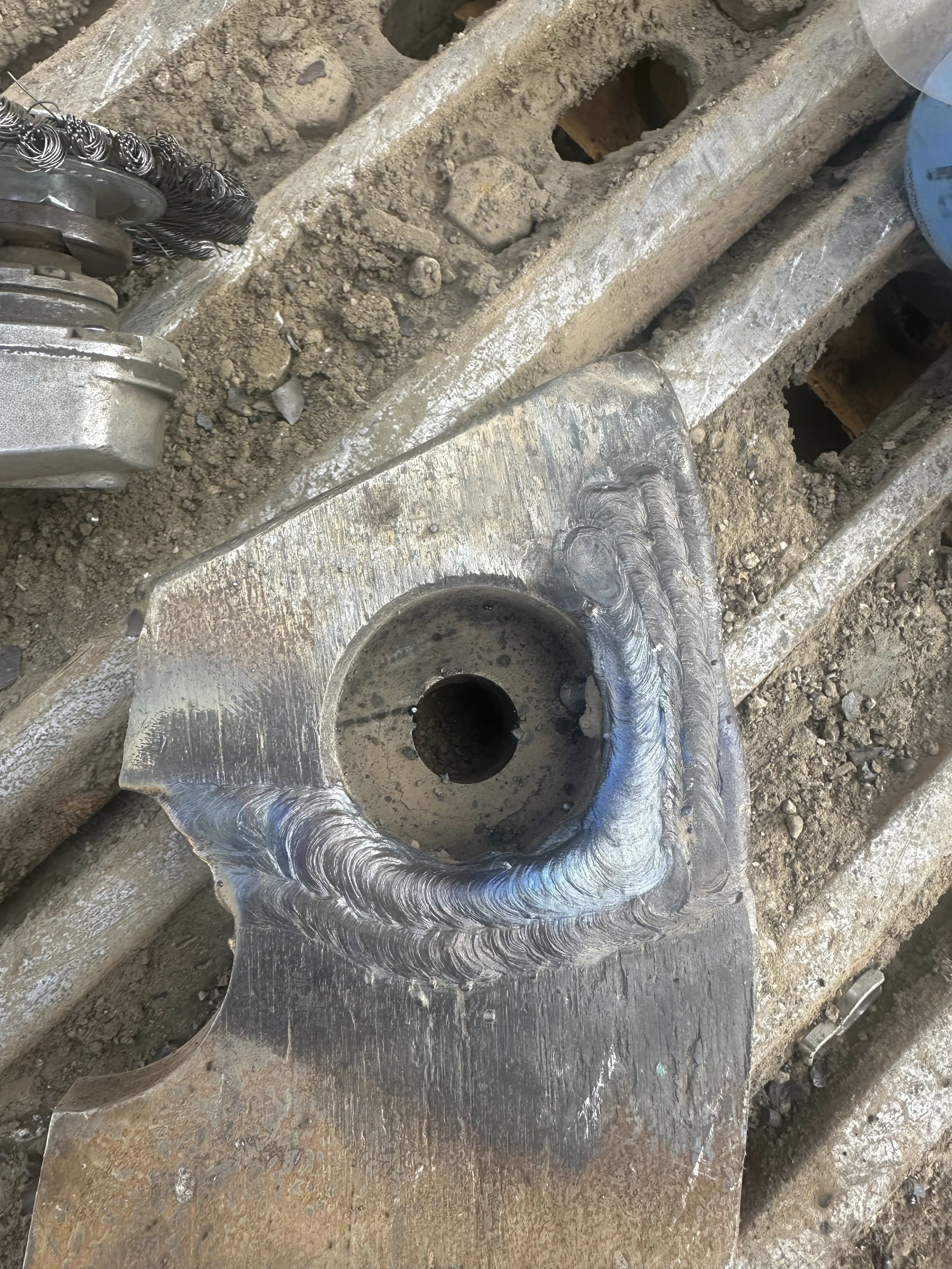 Close-up of a metal welding project showing a welded joint with weld beads on a metal part, with surrounding dirt and metal debris.