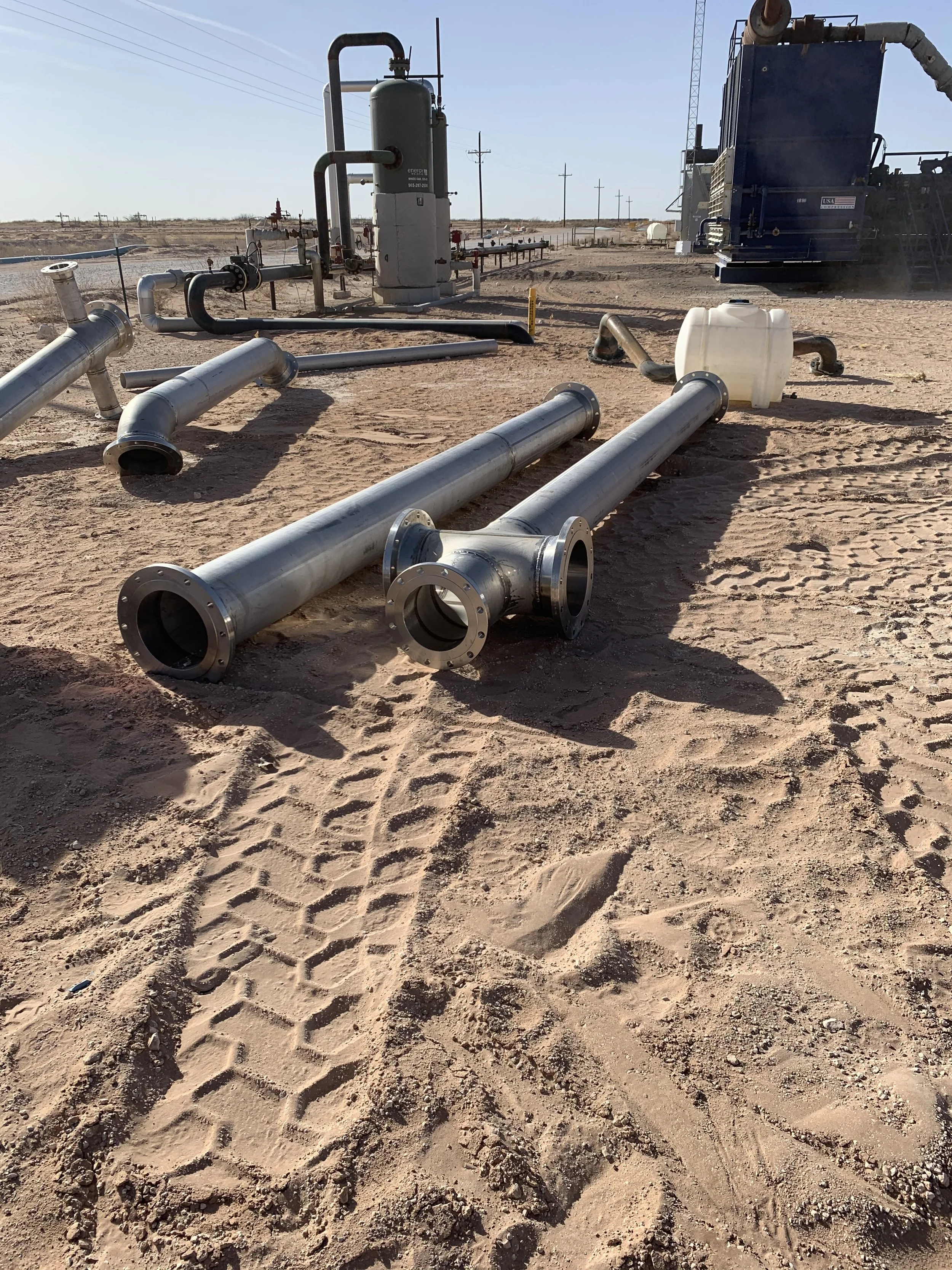 Construction site in a desert landscape with stainless steel pipe fabrication laying on the sand | John 6:9 Welding Company LLC | Sedalia, MO