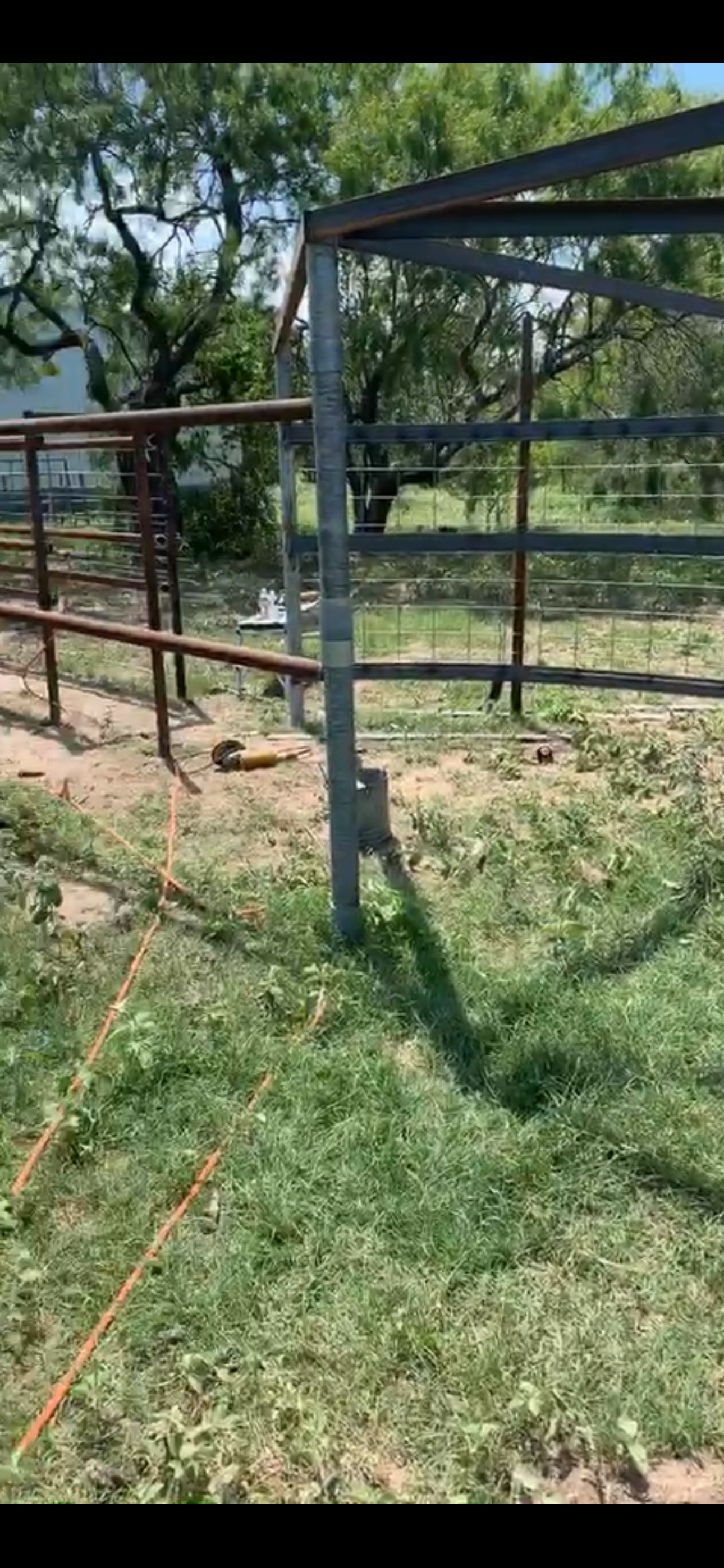 Partially constructed metal fence with green grass and trees in the background.