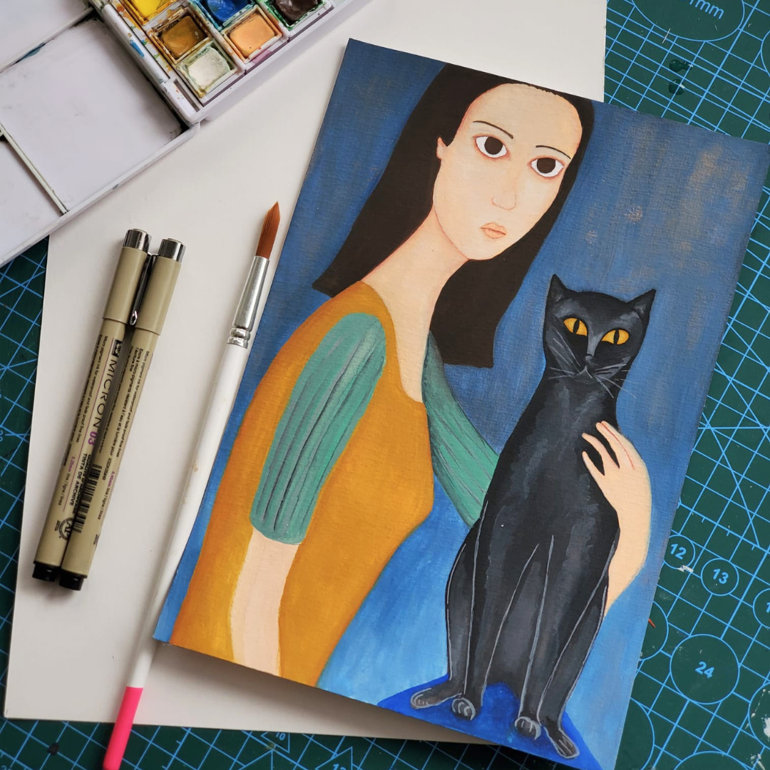 Hand-painted portrait of a woman holding a black cat, surrounded by watercolor paints, markers, and brushes