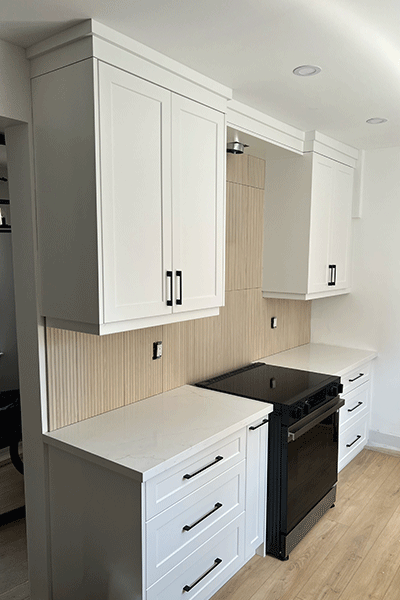 Kitchen with white cabinets, black handles, white countertop, black stove, wooden flooring, and beige tiled backsplash.