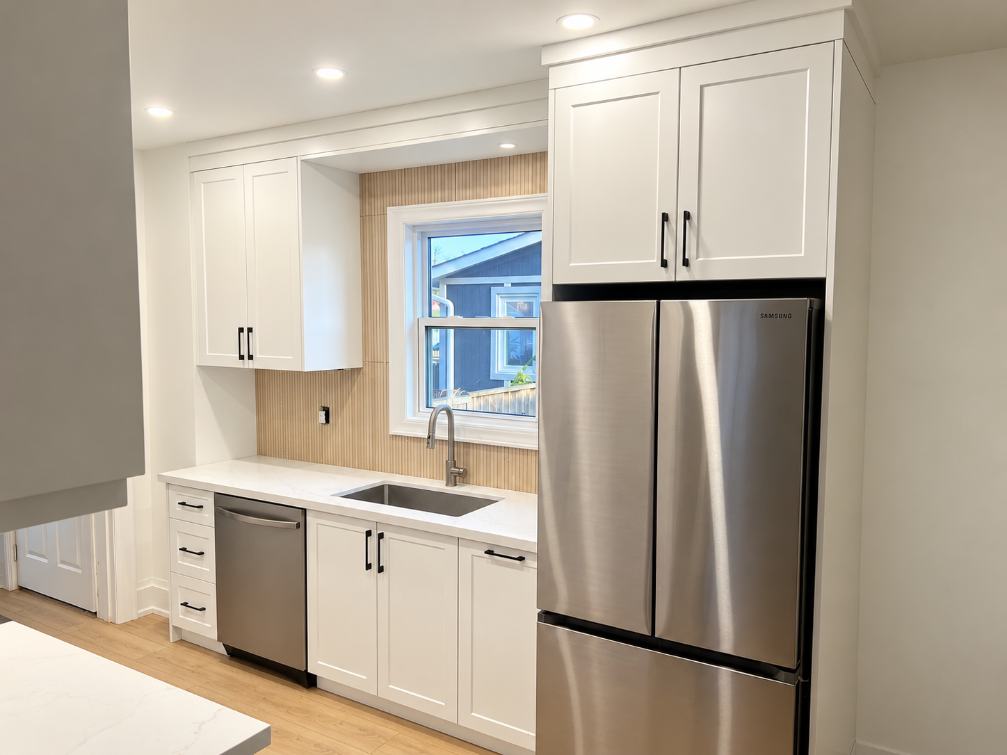 Modern kitchen with white cabinets, stainless steel appliances, a window above the sink, and light wood flooring.