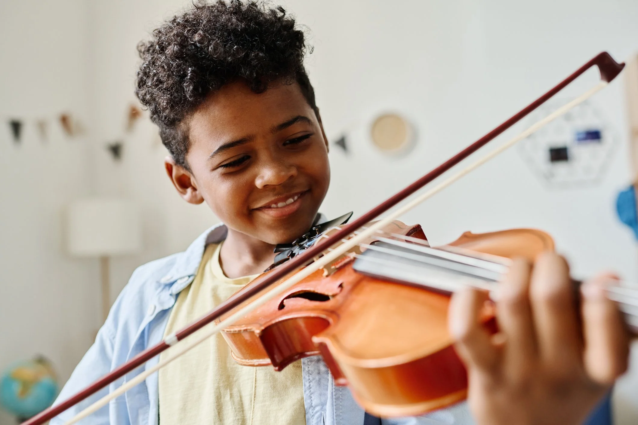 A young boy playing a violin, smiling as he looks at the instrument.