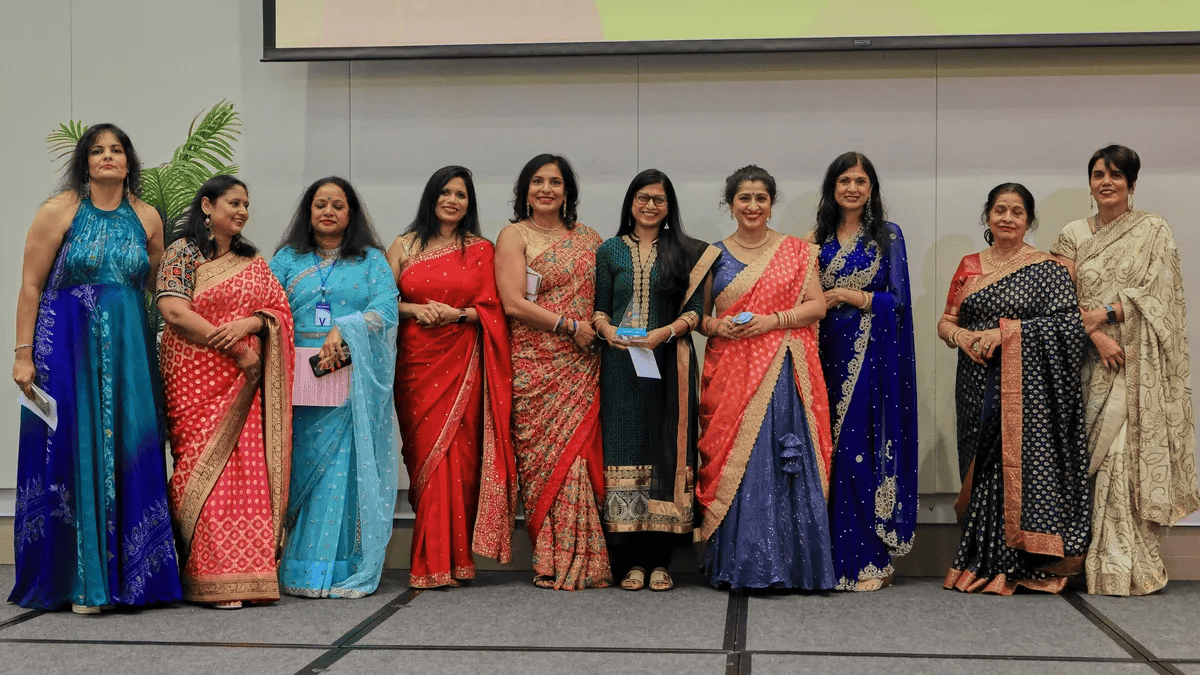 Ten women dressed in colorful sarees standing on a stage at a formal event.