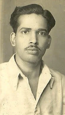 Black-and-white portrait of a young man with dark hair, mustache, wearing a collared shirt and a jacket over his shoulder.