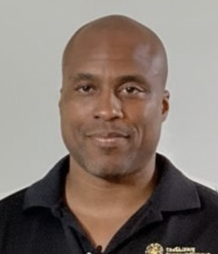 A portrait of a bald man with a slight smile, wearing a black collared shirt.