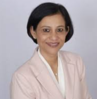 Professional portrait of a woman with short black hair, wearing a light pink blazer and white blouse, smiling against a plain gray background.