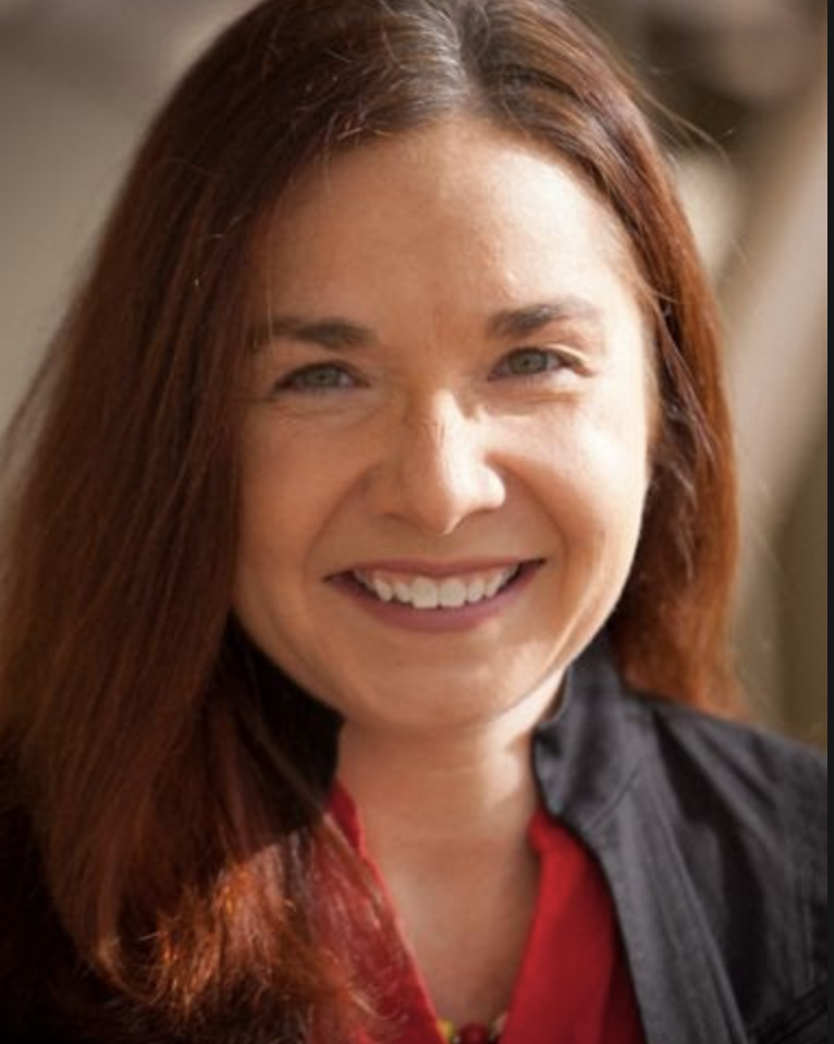 Close-up of a woman with long red hair smiling, wearing a black jacket and red top.