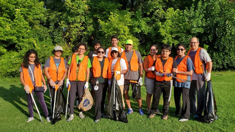 Group of people dressed in orange vests participating in a community cleanup in a park, holding trash bags and litter pickers.