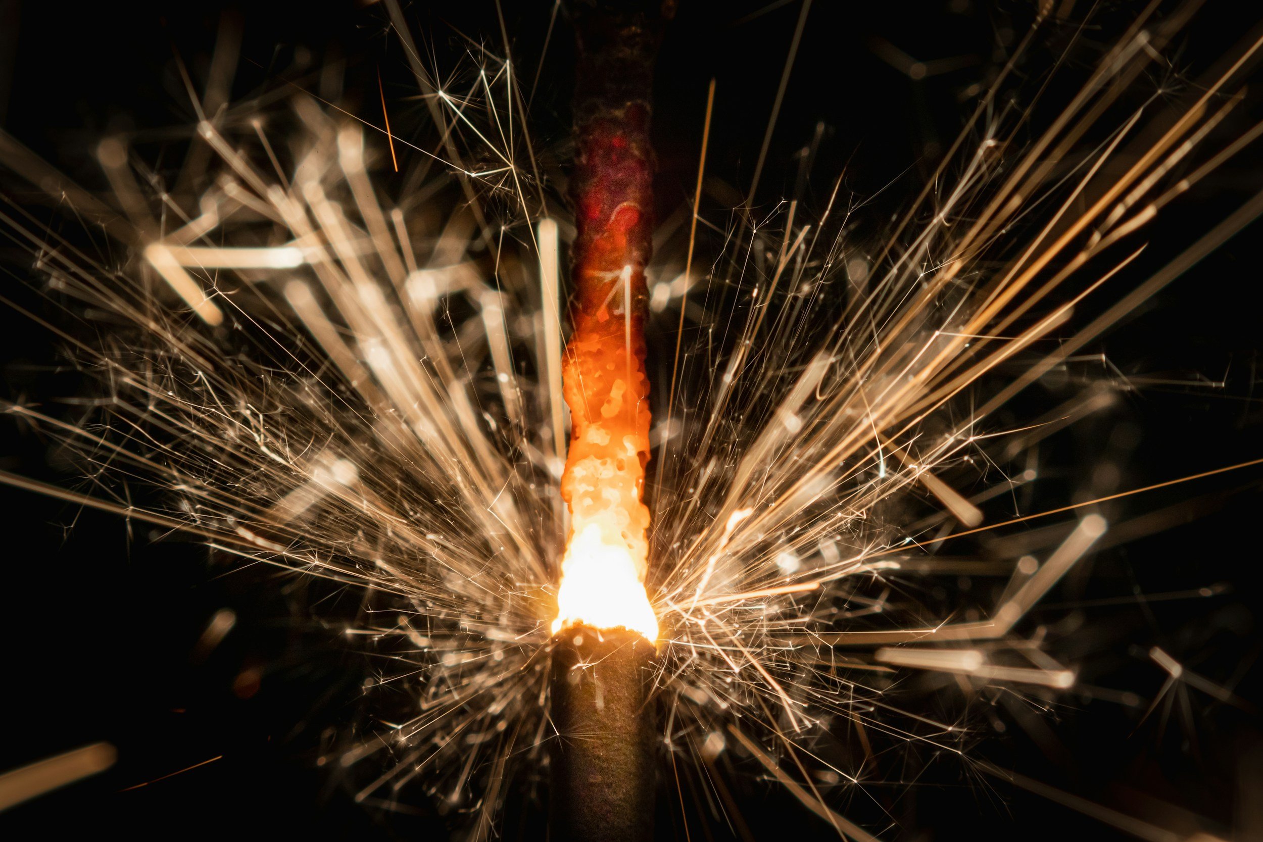 A sparkler emitting bright sparks against a dark background.