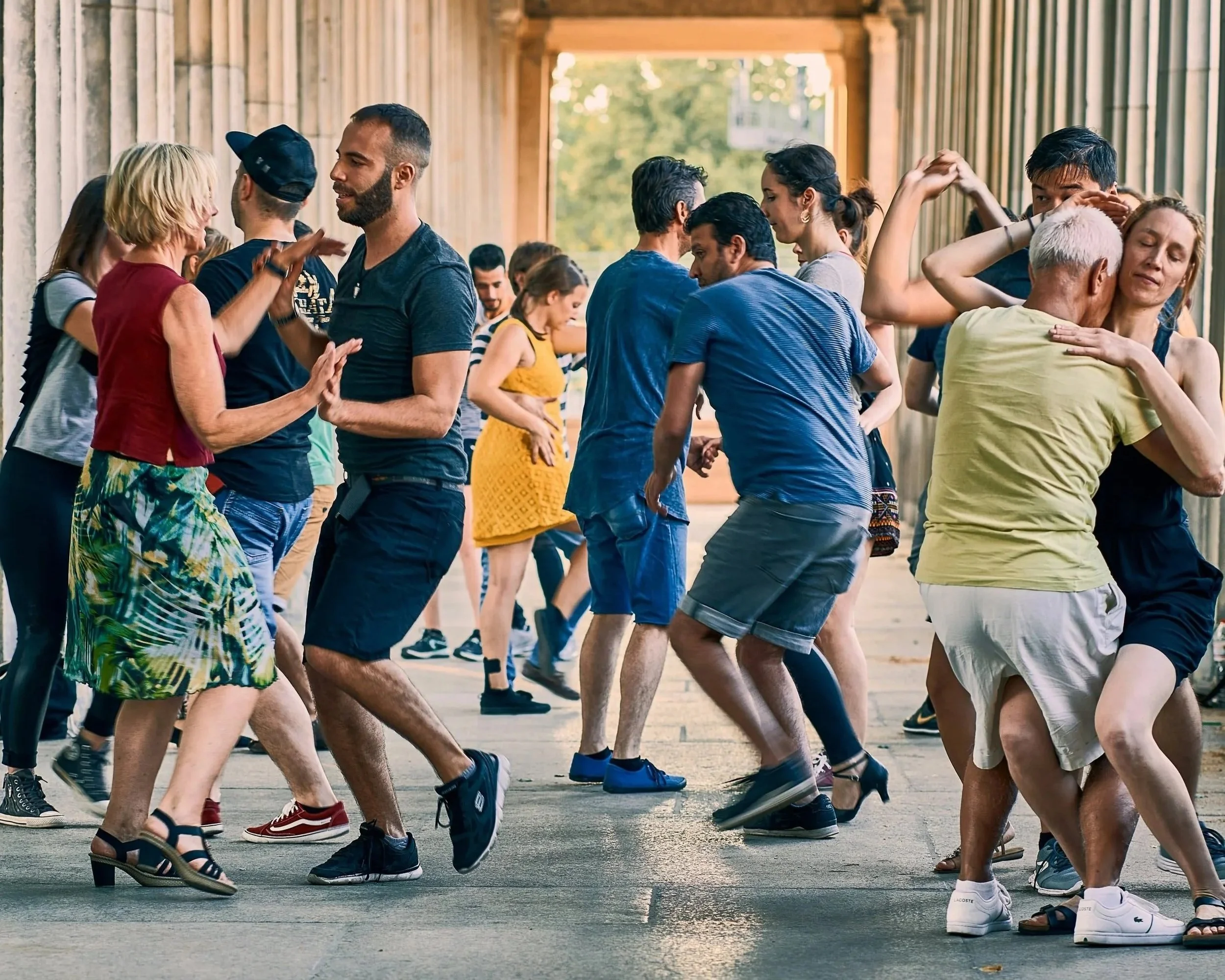 People dancing closely together outdoors, enjoying a social event or dance class under a wooden structure with a natural background.