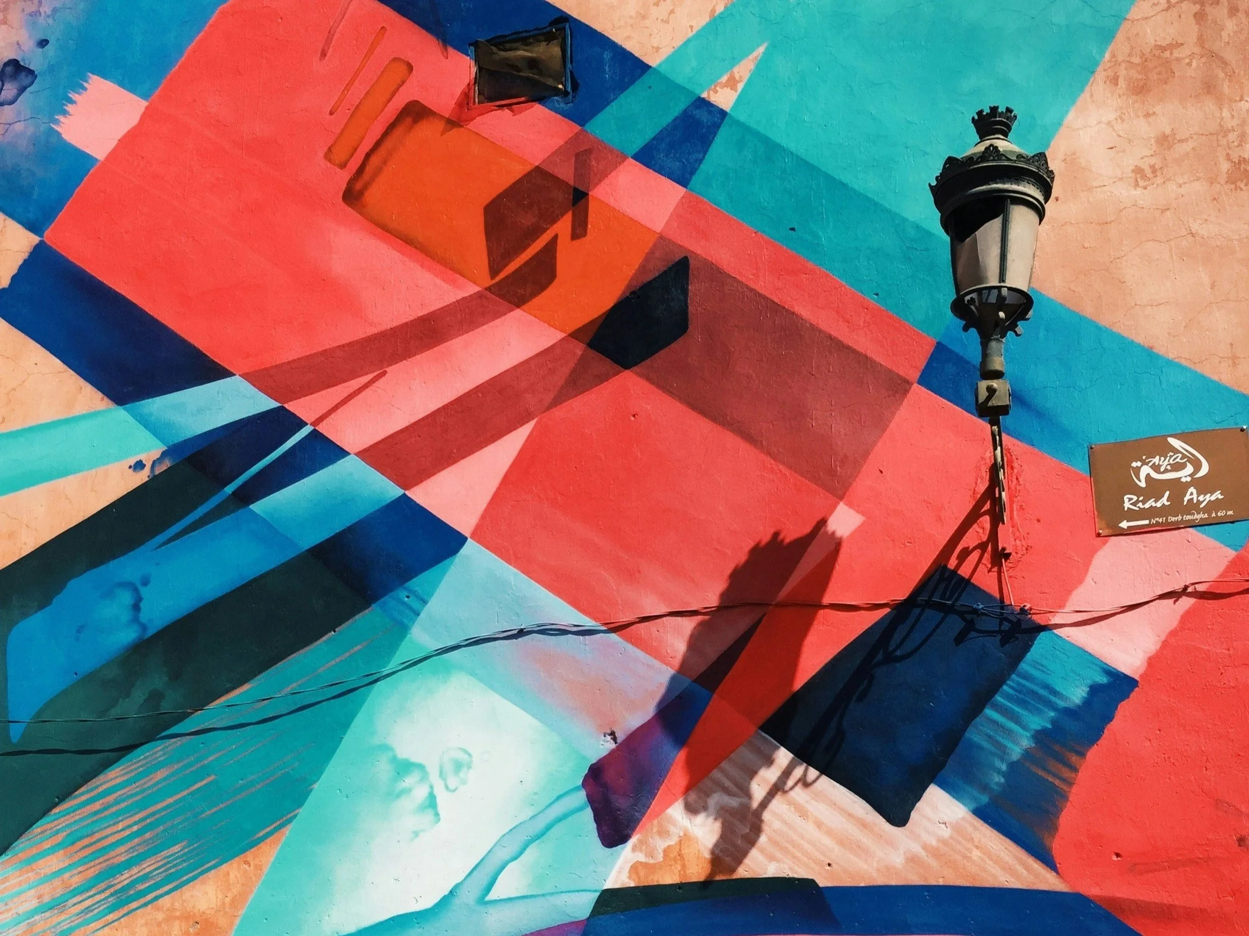 Colorful abstract mural painting on a wall featuring geometric shapes, vibrant colors, and a vintage streetlamp mounted on the wall.