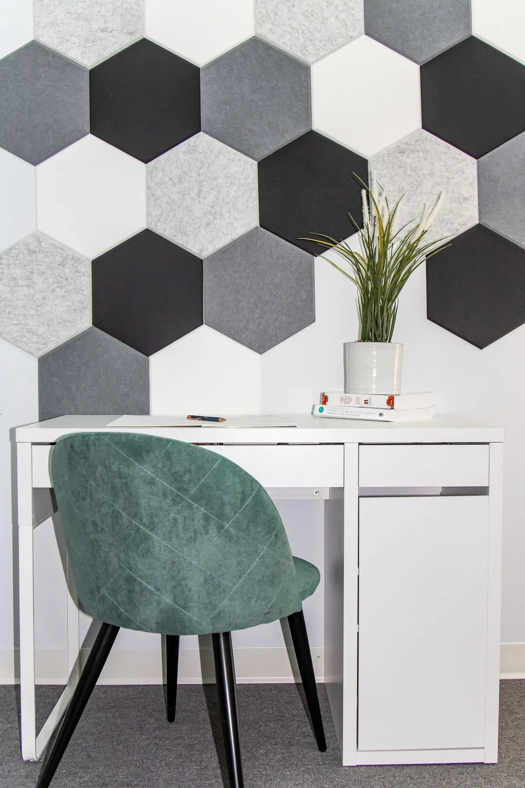 Modern workspace with a white desk, a green upholstered chair, a potted plant, and a wall with hexagonal tiles in shades of black, gray, and white.