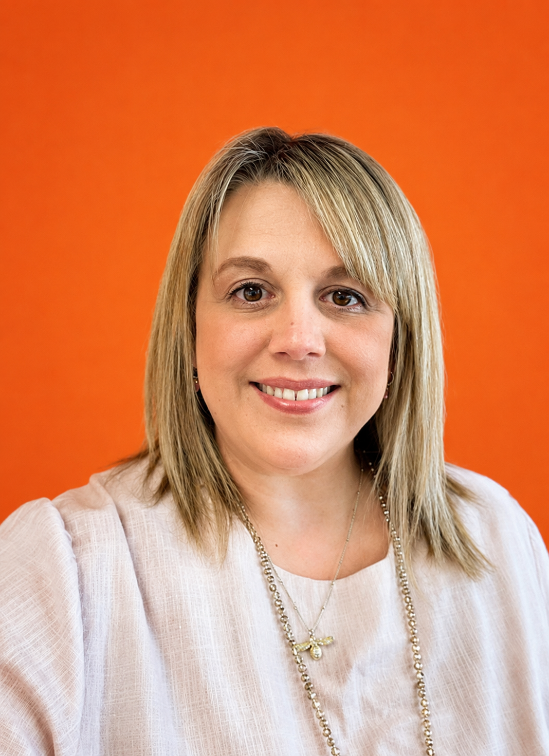 A woman with blonde hair smiling against an orange background.