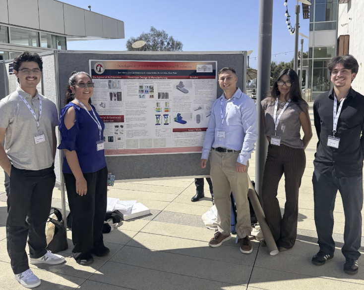 Group of five people standing in front of a research poster outdoors, with some tree and building visible in the background.