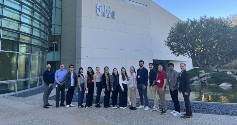 Group of 14 people standing outside Masimo building near a pond and trees.