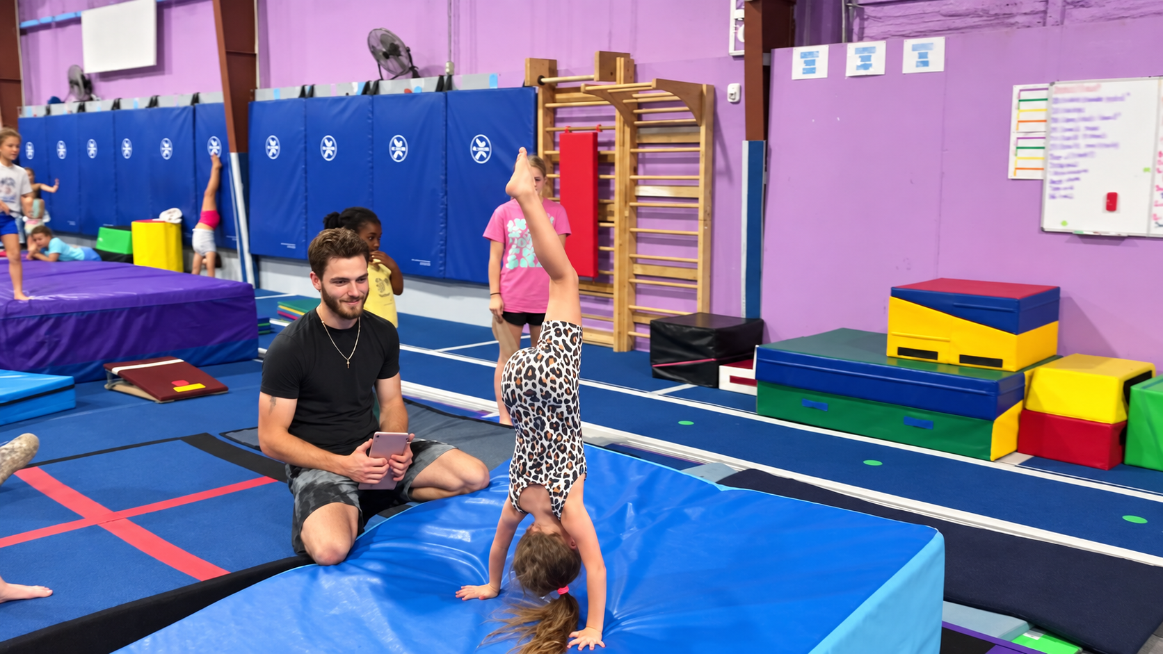 Young children practicing gymnastics on various equipment in a gymnasium decorated with American and Arkansas flags. Hot Springs Gymnastics | 112 Bluestone Ct. Hot Springs, Arkansas 71901