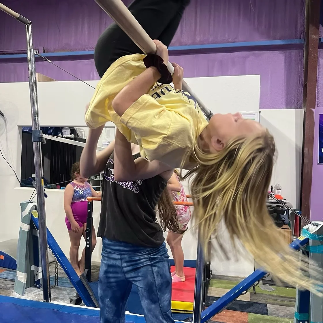 A group of children and two women sitting on a purple padded mat inside a gym. Hot Springs Gymnastics | 112 Bluestone Ct. Hot Springs, Arkansas 71901