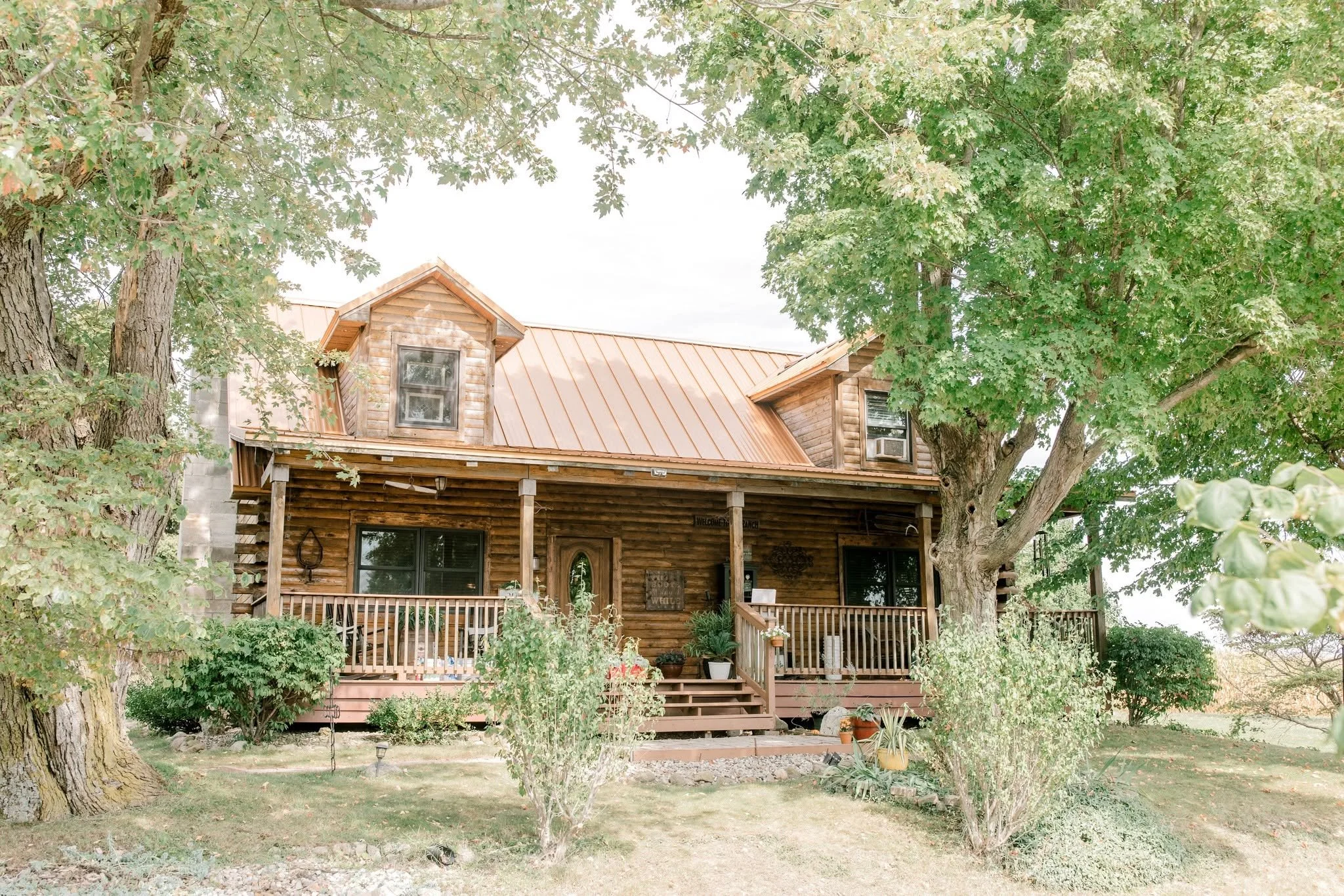 A wooden house with a porch surrounded by trees and greenery.