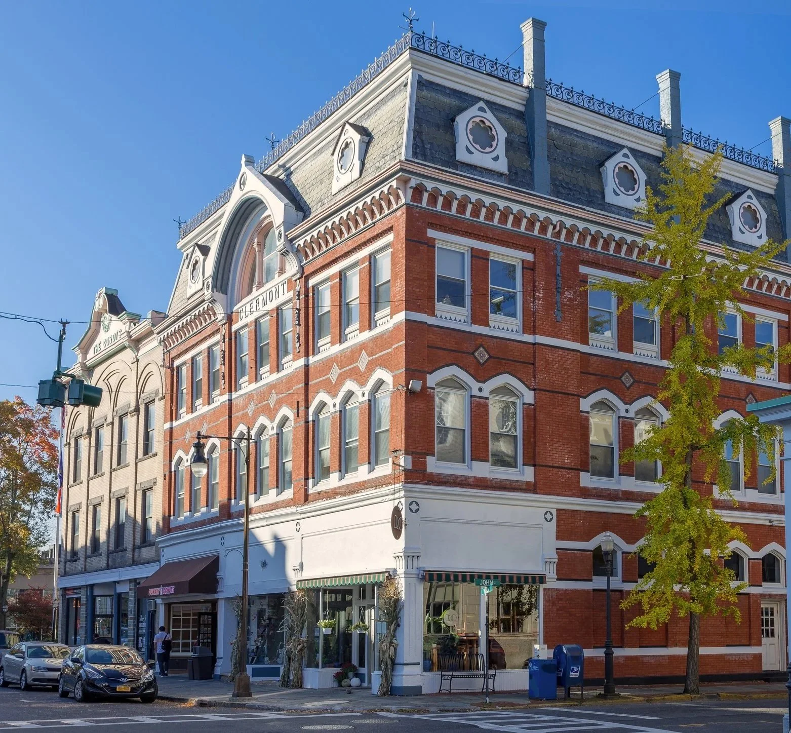 Sycamore Street Advisors is located in Kingston, NY. A multi-story brick building with ornate architectural details on a city street, featuring ground-floor shops and greenery, under a clear blue sky.