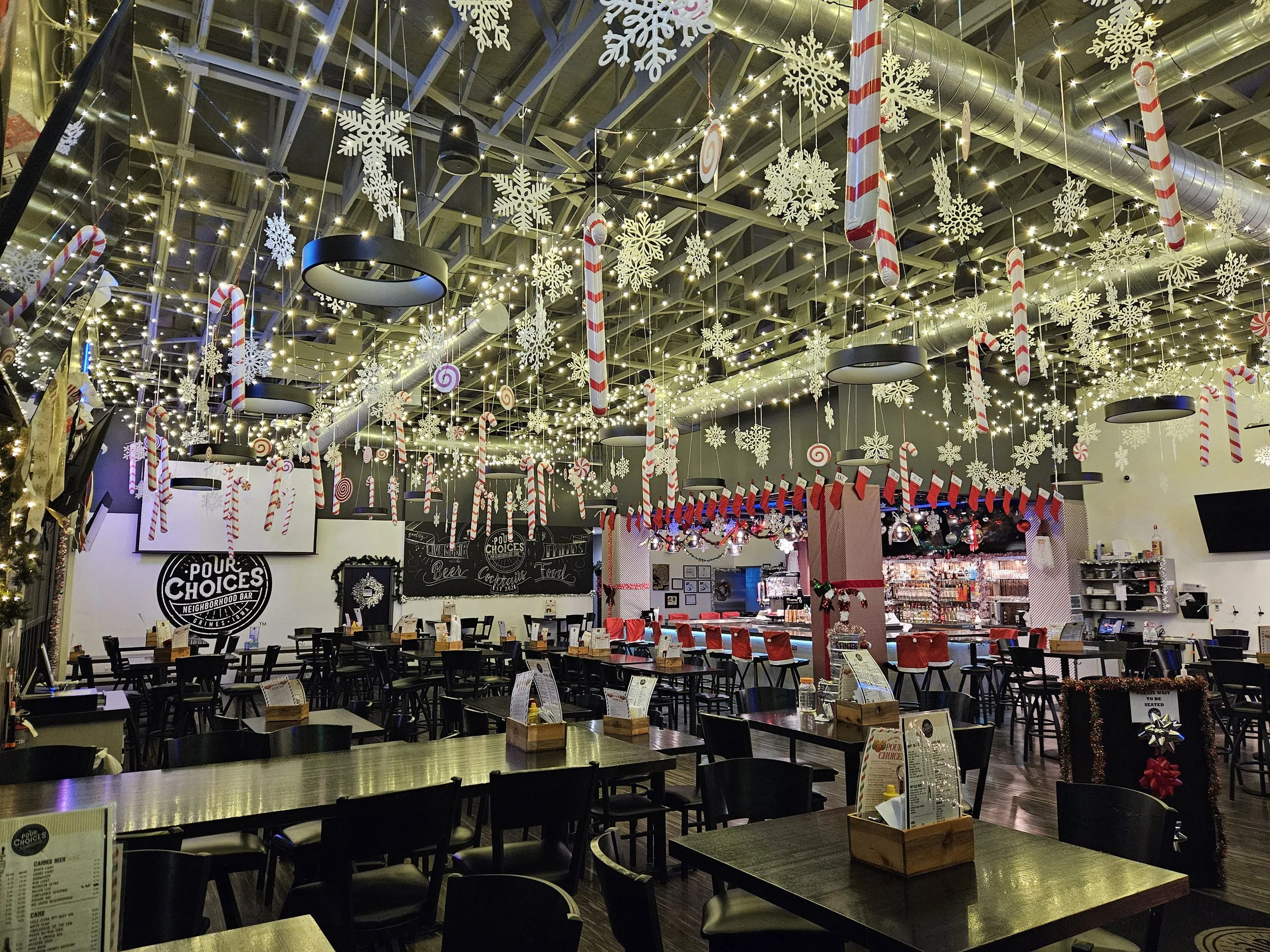 Indoor restaurant decorated with Christmas holiday decorations including white snowflakes, candy canes, red stockings, and string lights hanging from the ceiling.