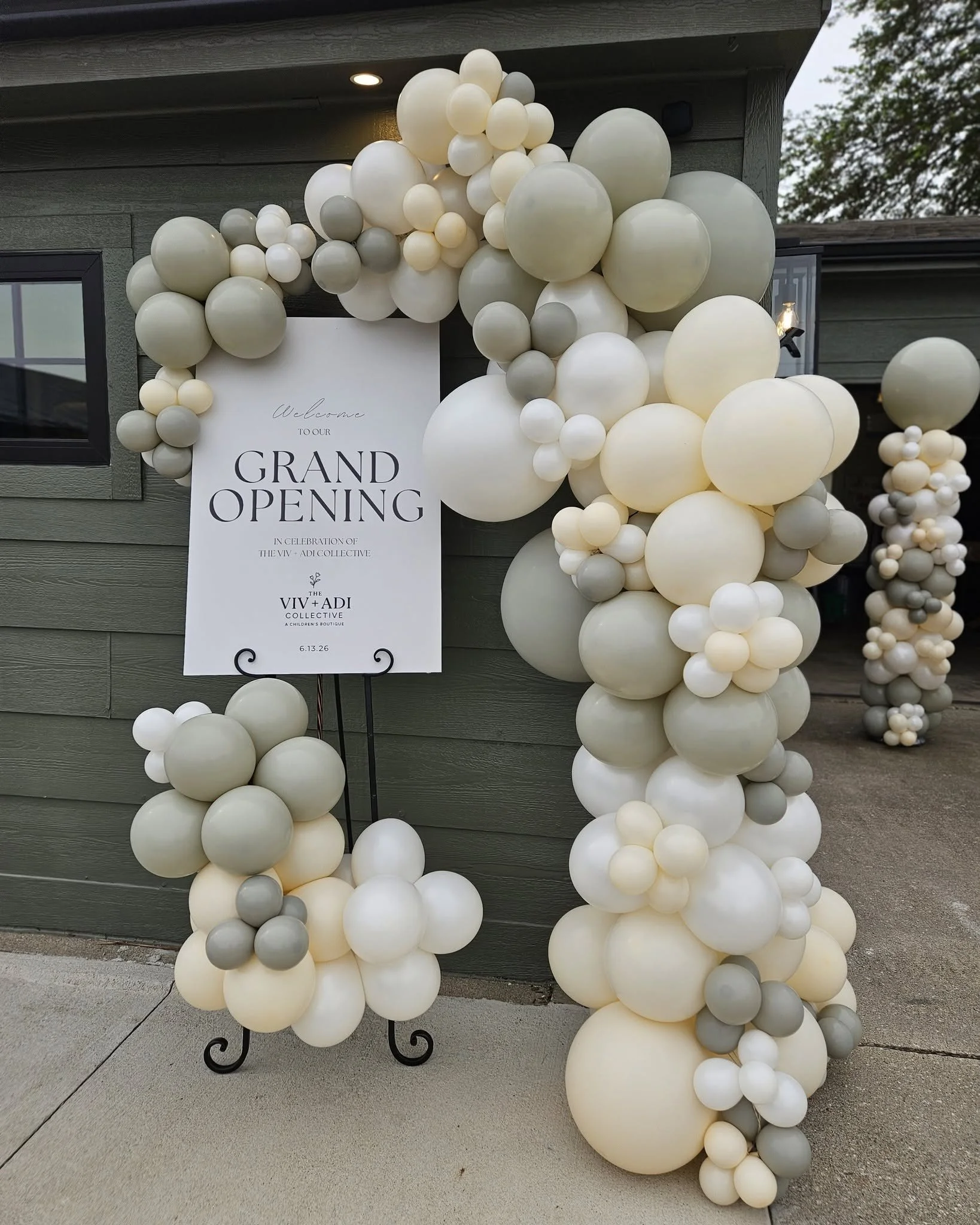 Balloon arch in white, cream, and gray colors decorated around a sign for a grand opening event.
