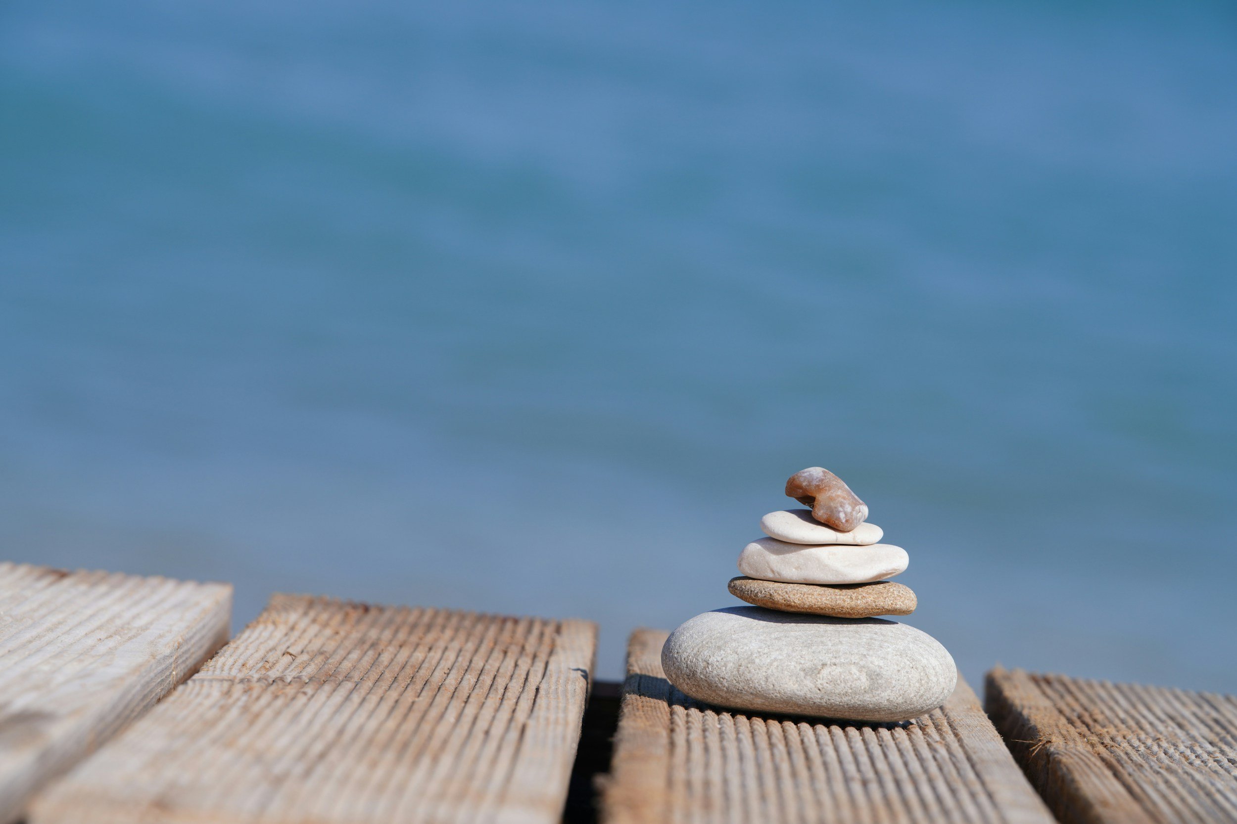 A stack of seven white and brown rocks on a wooden surface with a blue sky background.
