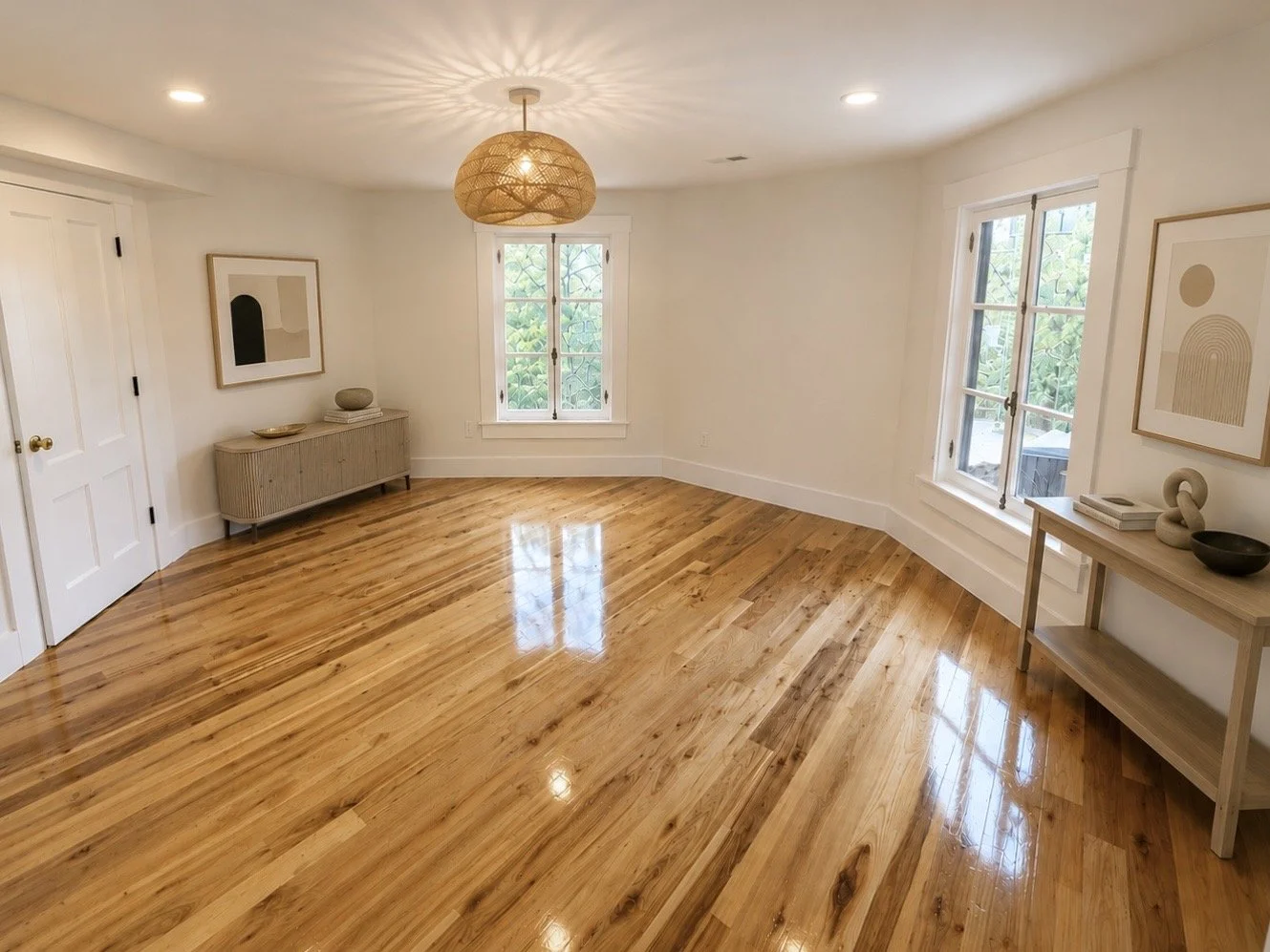 A spacious, empty living room with glossy hardwood floors, white walls, two large windows, minimalist decor, and a woven pendant light.
