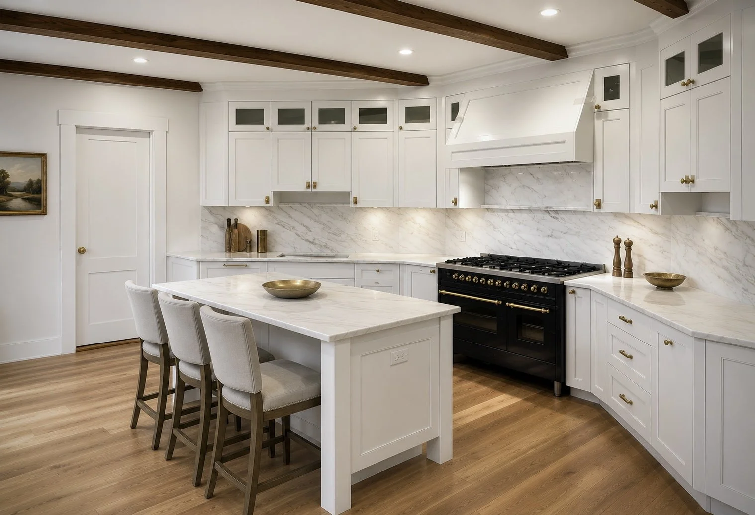 Modern kitchen with white cabinets, marble countertops, and a black stove, with a kitchen island and beige chairs, wood floors, and wood ceiling beams.