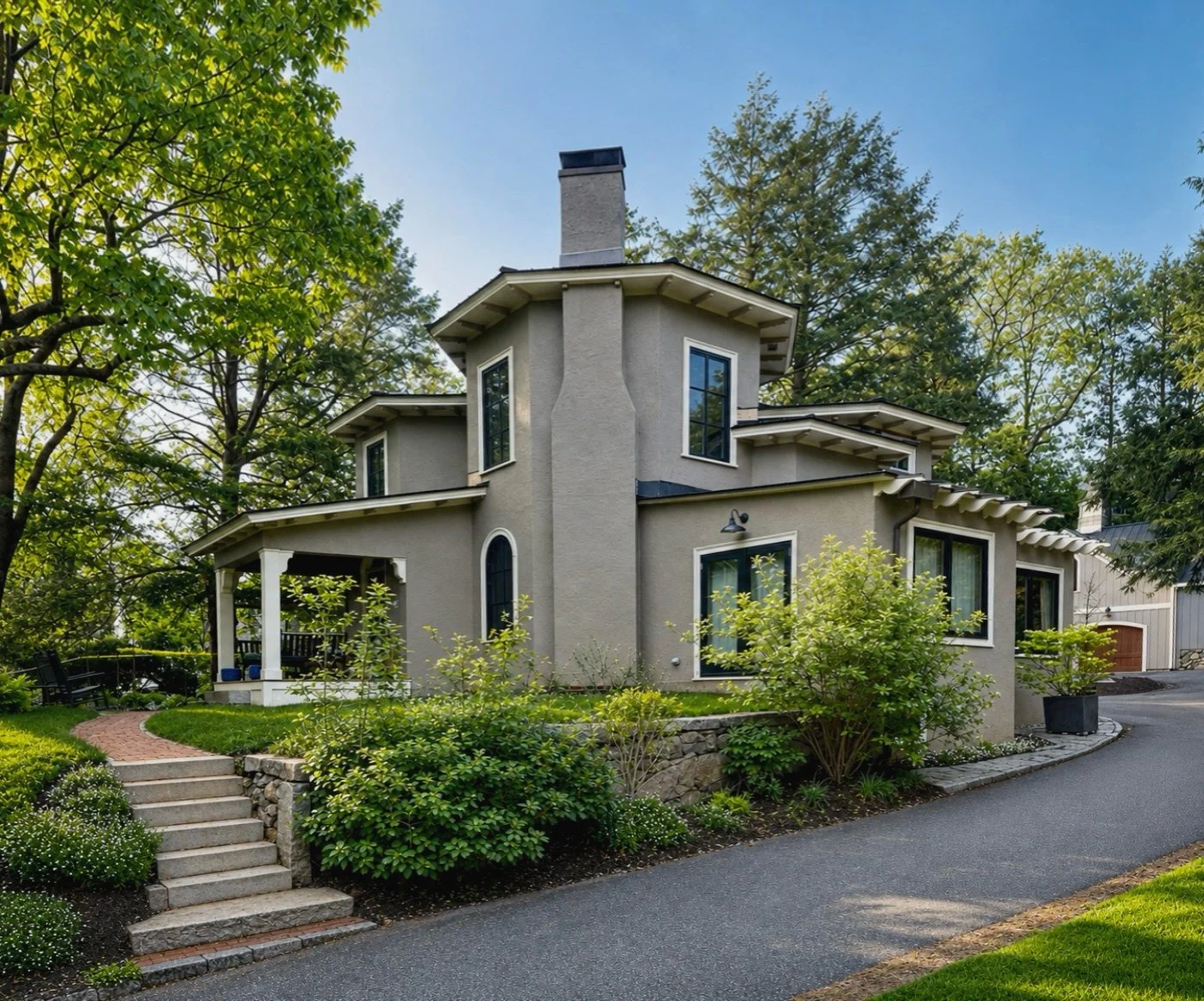 A two-story gray house with black and white trim, surrounded by green trees and shrubs, with a curved driveway and a staircase leading to the front porch.