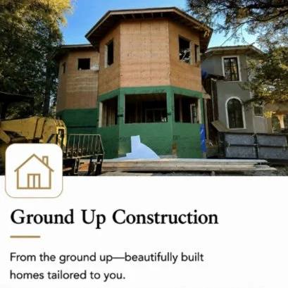 Under construction view of a new, multi-story house with wooden framing and green protective sheathing, surrounded by trees.