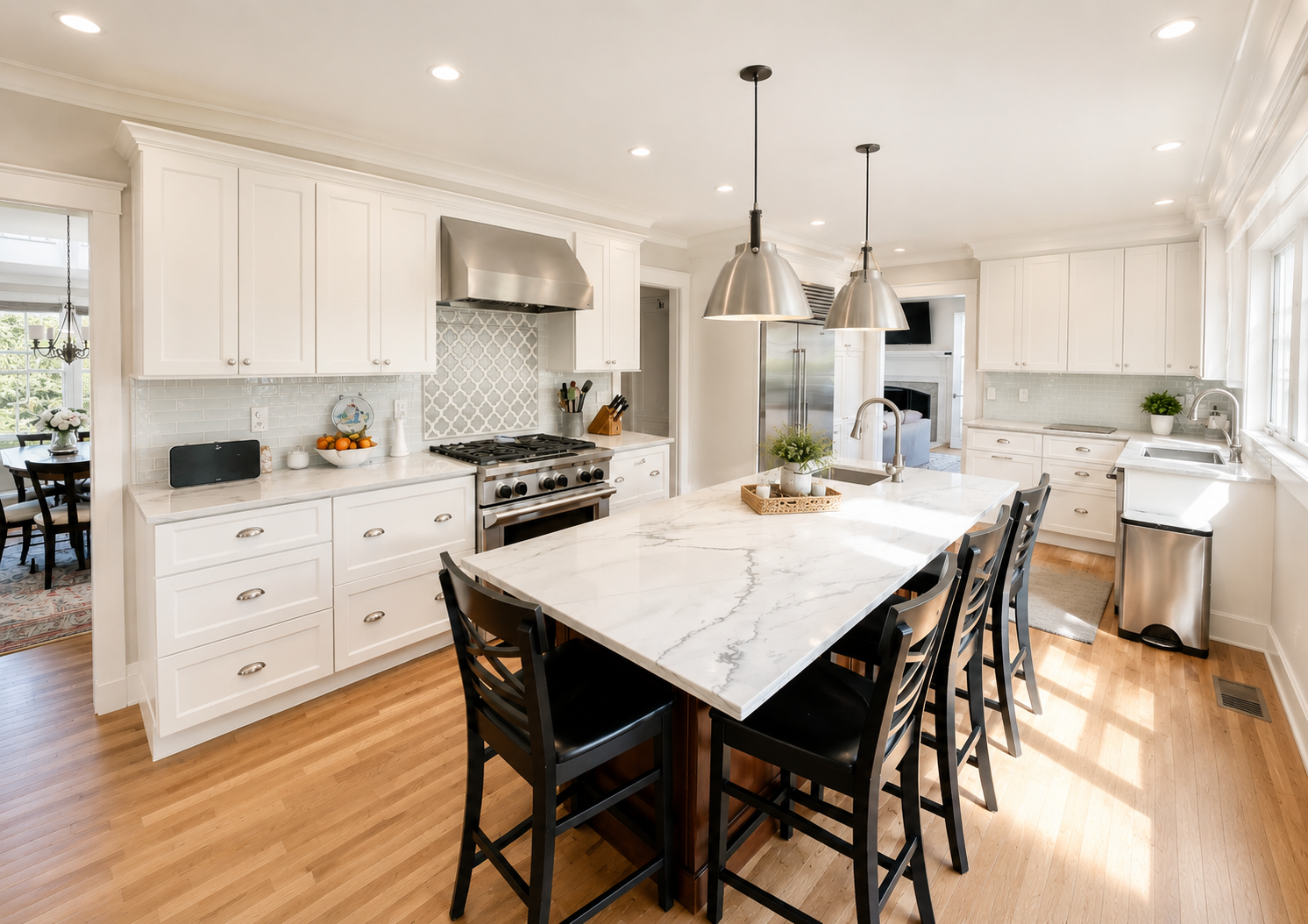 Bright kitchen with white cabinets, marble countertop island, black chairs, stainless steel appliances, and hardwood flooring.