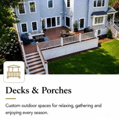 Outdoor wooden deck with seating area, surrounded by white railing, attached to a blue house with white trim, overlooking a green grassy yard.