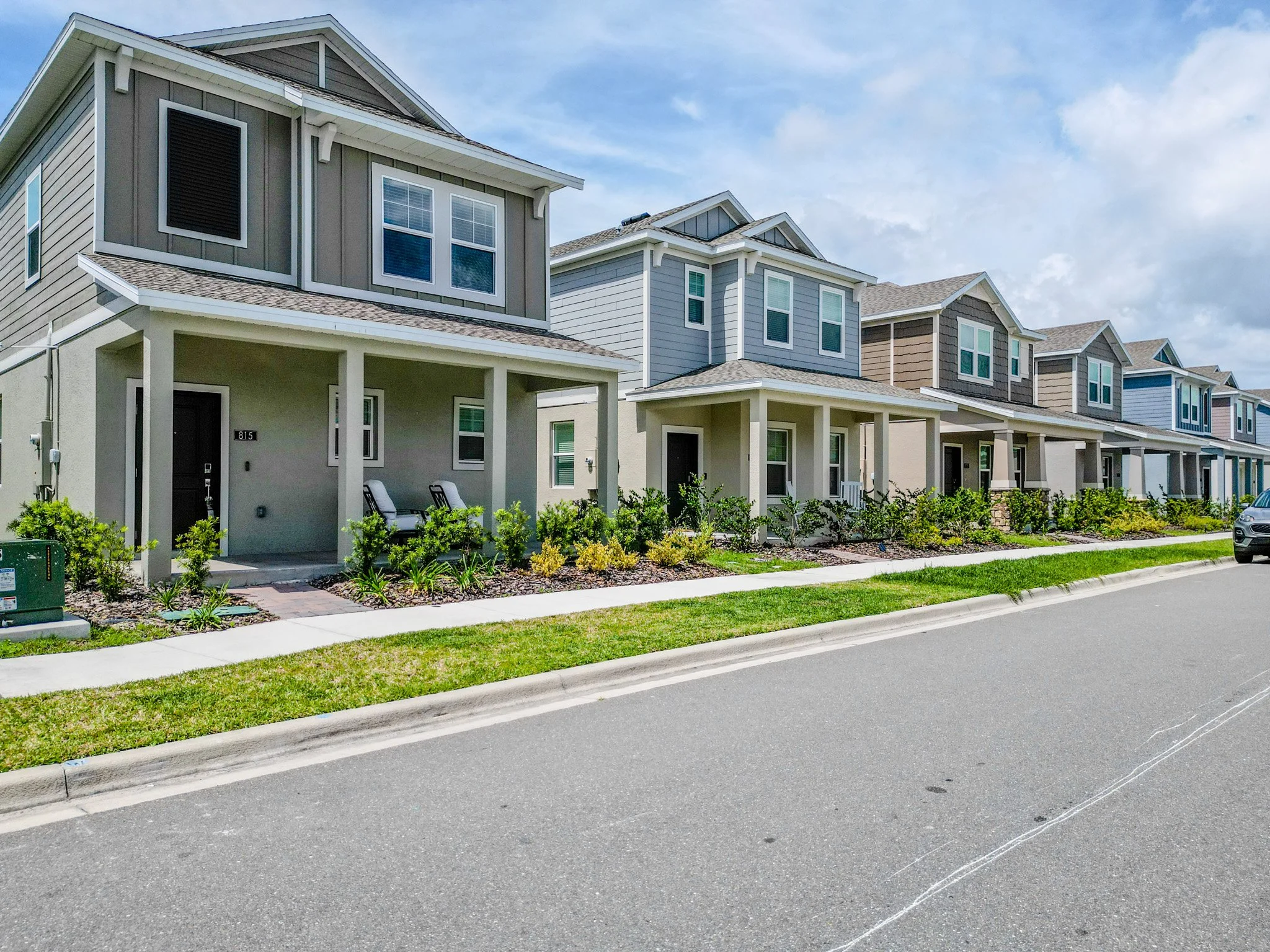 A row of modern townhouses with covered porches, multiple windows, and different exterior colors, situated along a street with a sidewalk and green landscaping at Rivington in DeBary, Florida