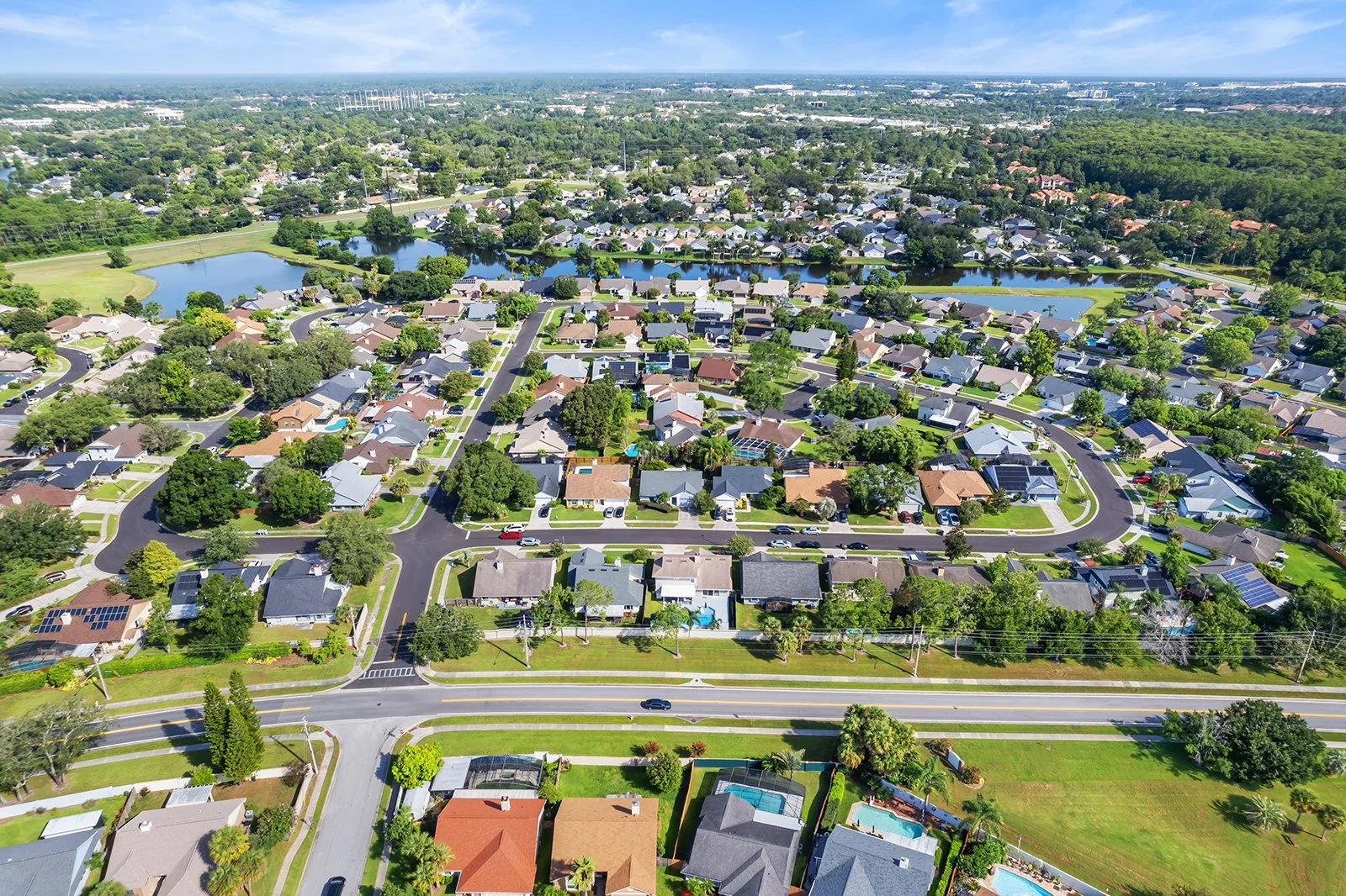 Aerial view of a suburban neighborhood with houses, streets, trees, lakes, and green spaces.